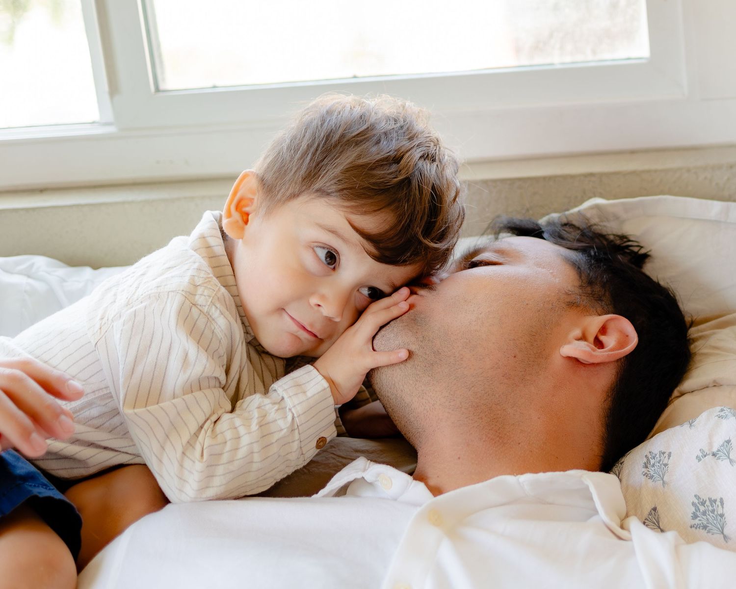 A couple shares a tender moment while resting together on a white bed.