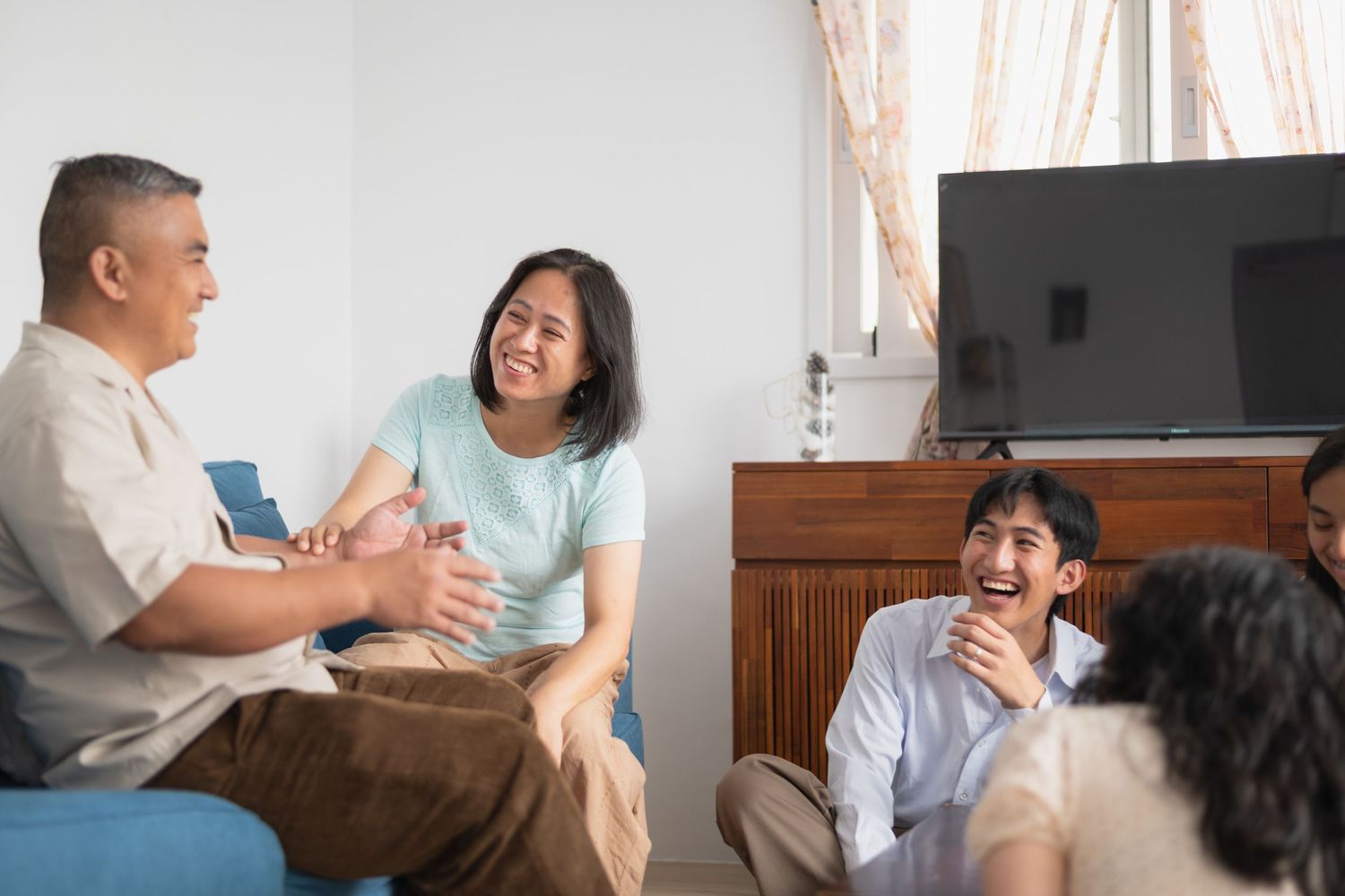Asian family laughing and bonding together in a cozy living room with a TV in the background.