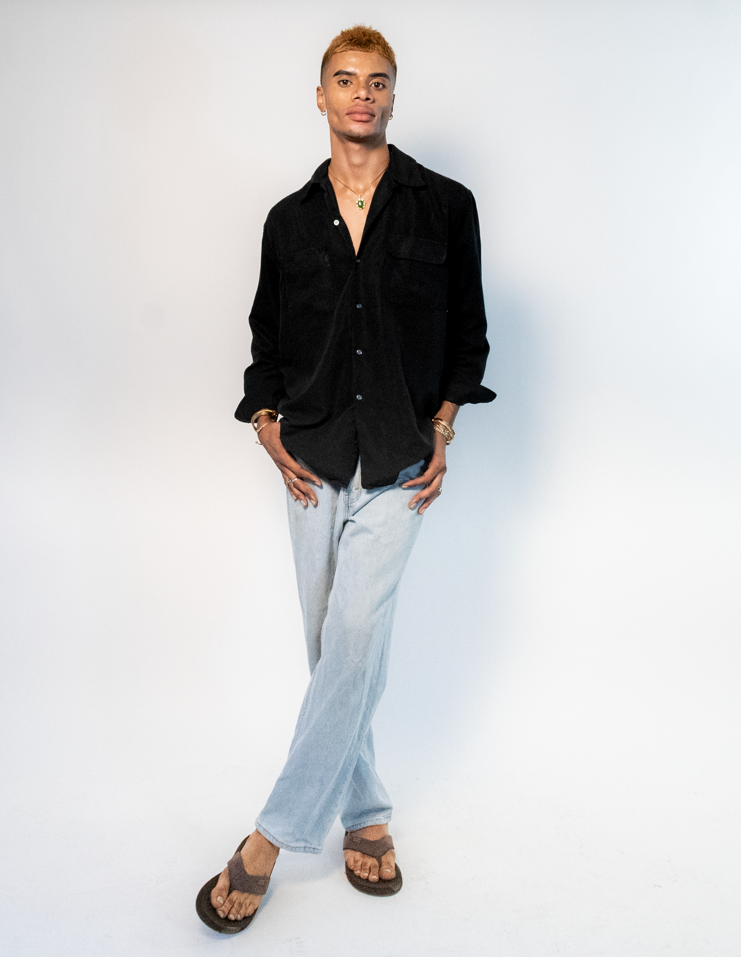 A person wearing a black button-down shirt and light gray pants poses in four different casual stances against a white background.