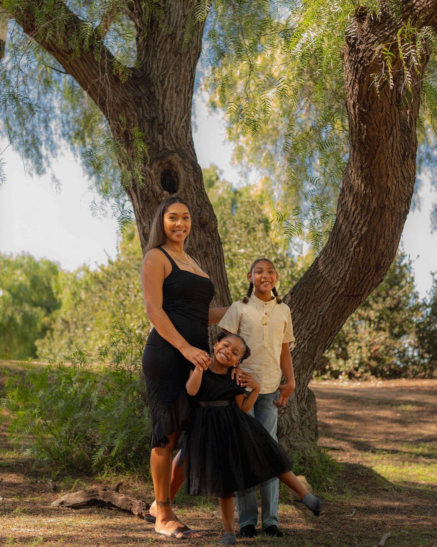 A family poses together for outdoor portraits under a large tree in a natural setting.