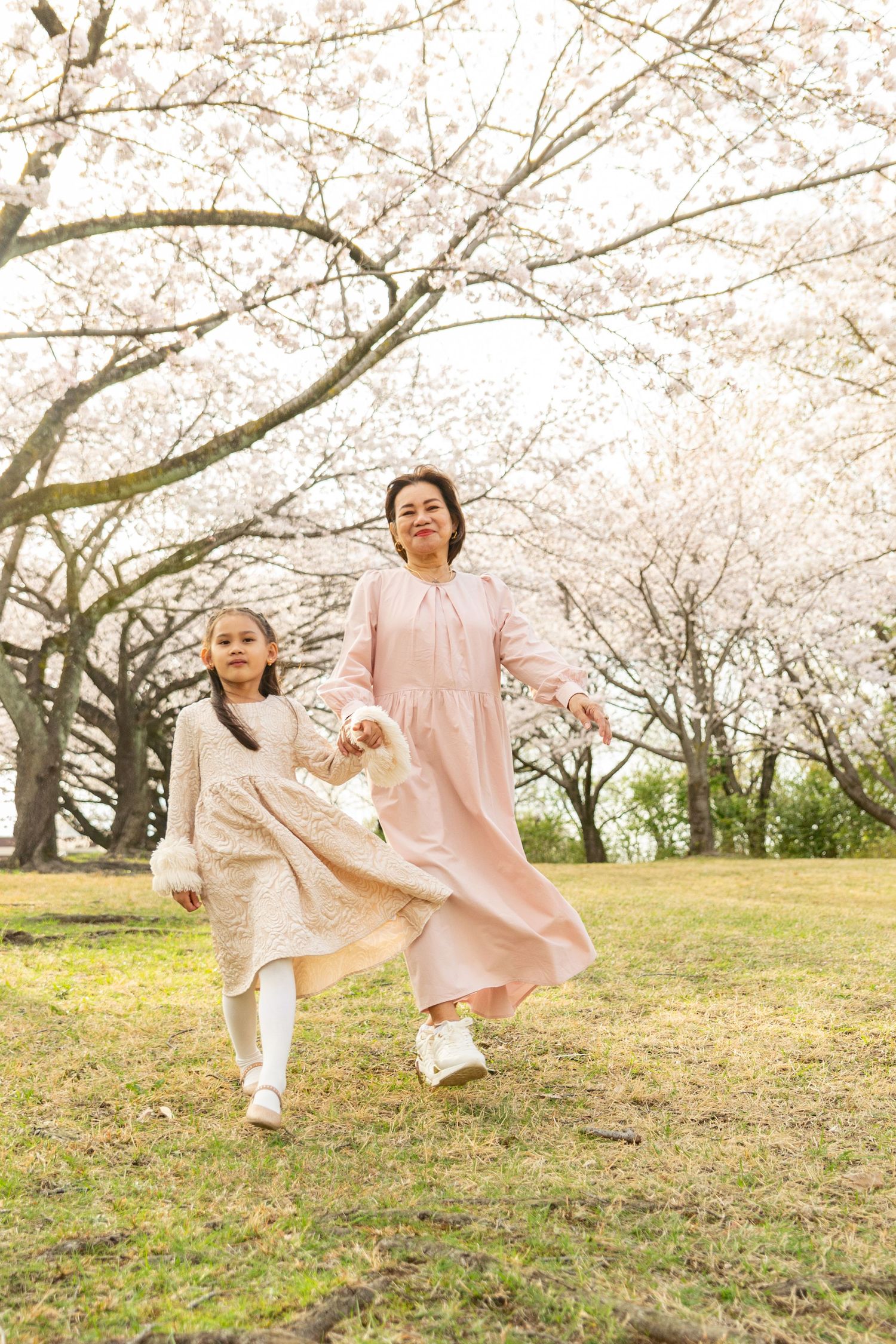 People enjoying spring day under blooming cherry blossom trees on grassy hillside in matching pink outfits.