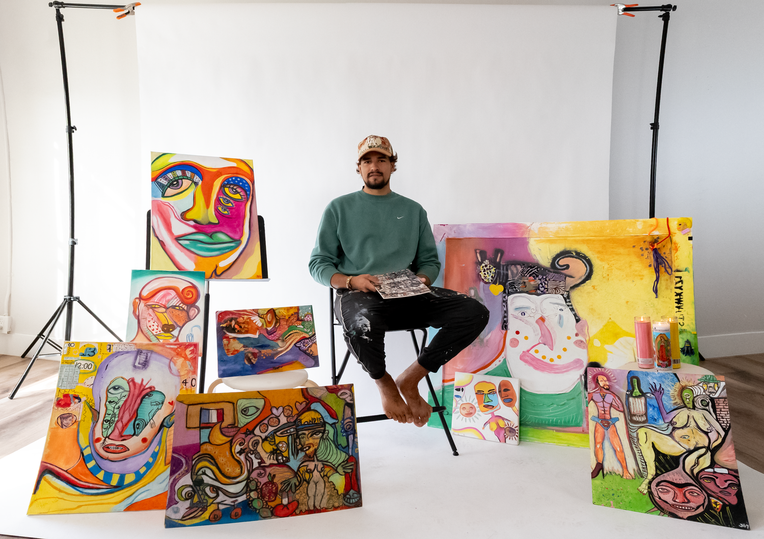 A panoramic view of colorful abstract paintings displayed in a studio with lighting equipment and an artist at work.