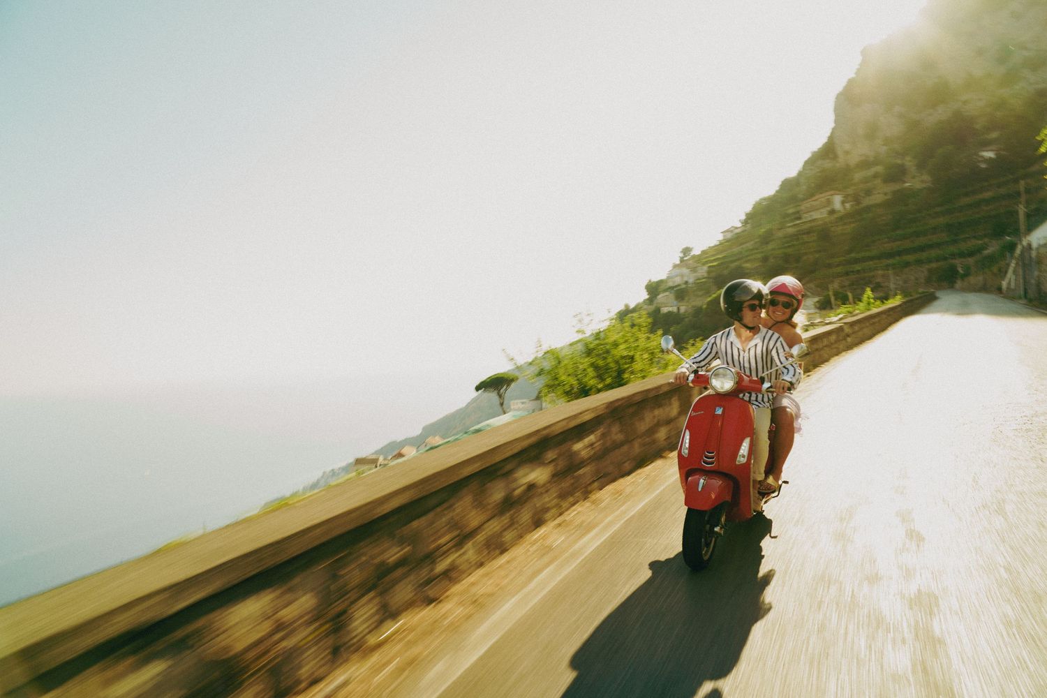 Guy and girl ride a red vespa down the streets during sunset along the Amalfi Coast in Italy.