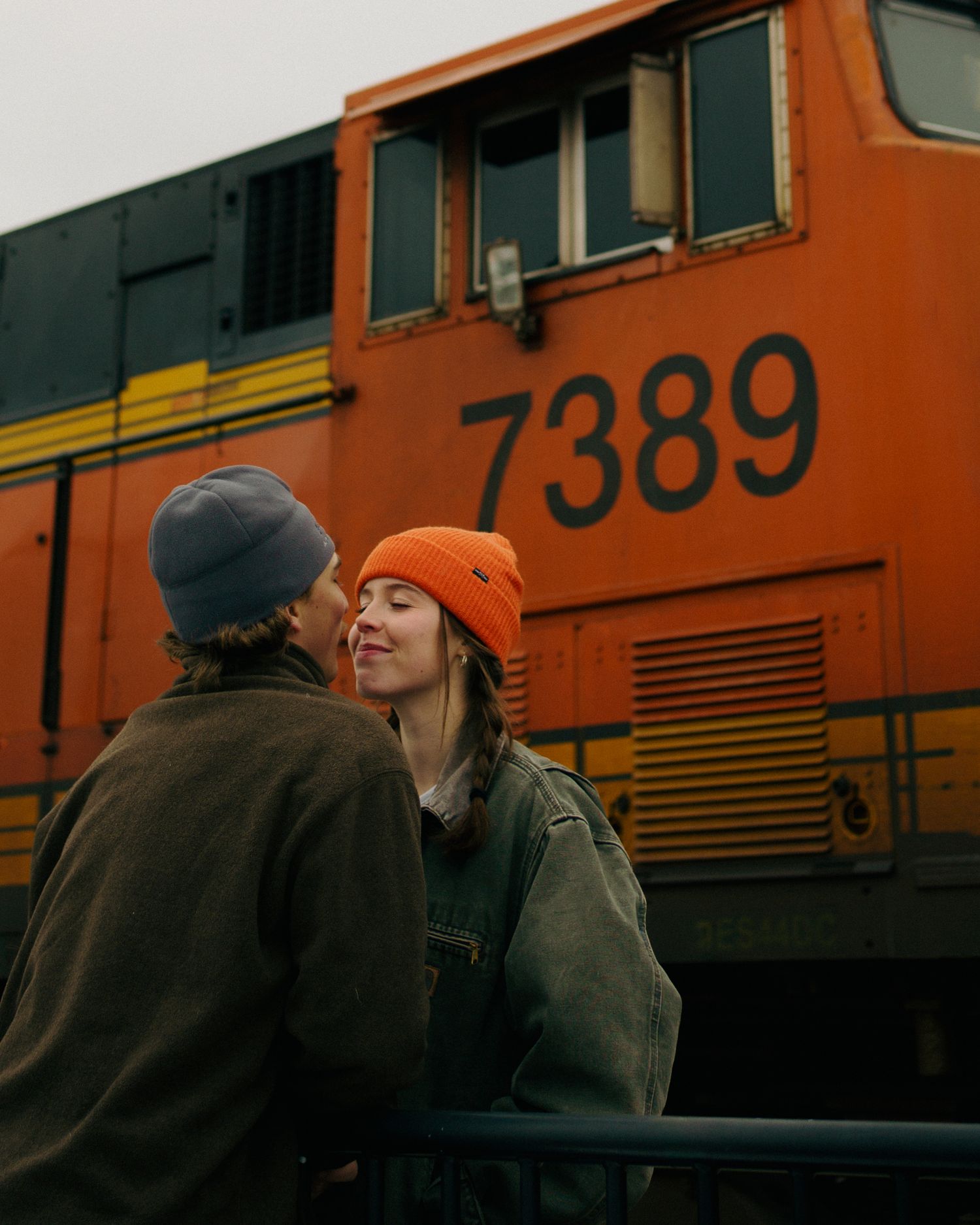 Couple lean in close in front of an orange train in downtown Whitefish, Montana.