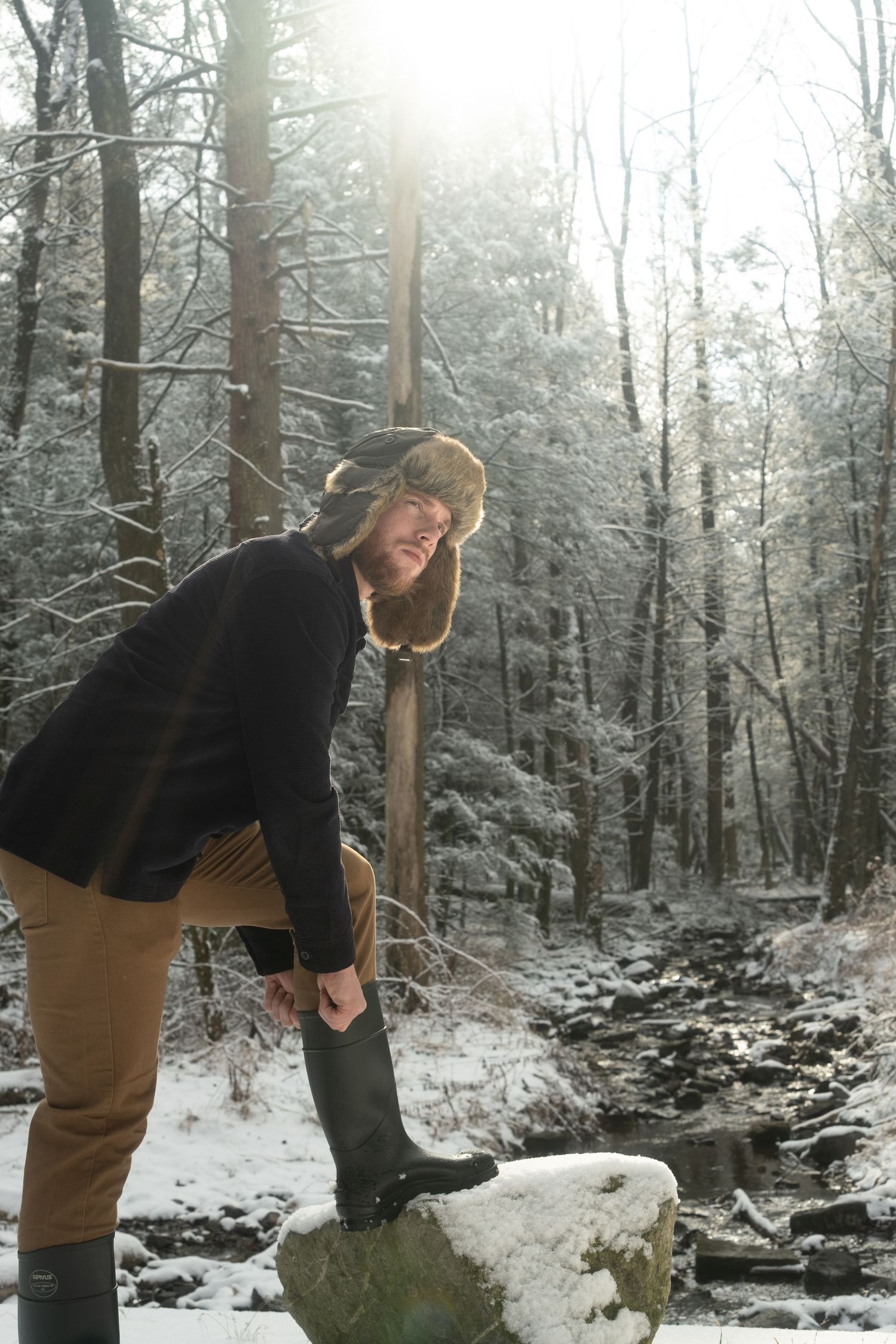 A sequence of four snowy winter forest scenes shows someone attempting to lift a large snow-covered rock.