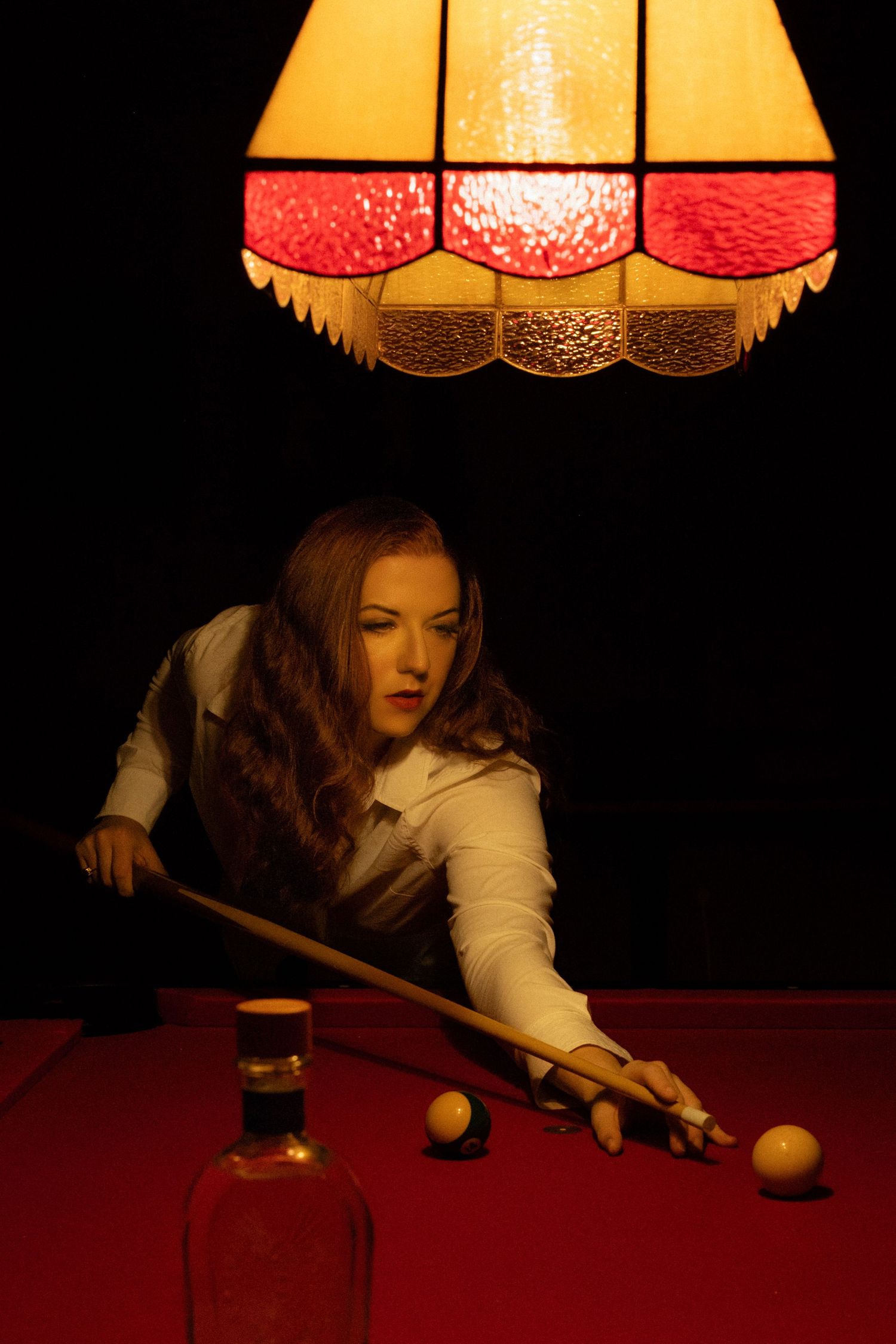 A person playing pool under a vintage red and yellow lamp in a dimly lit room with dramatic lighting.