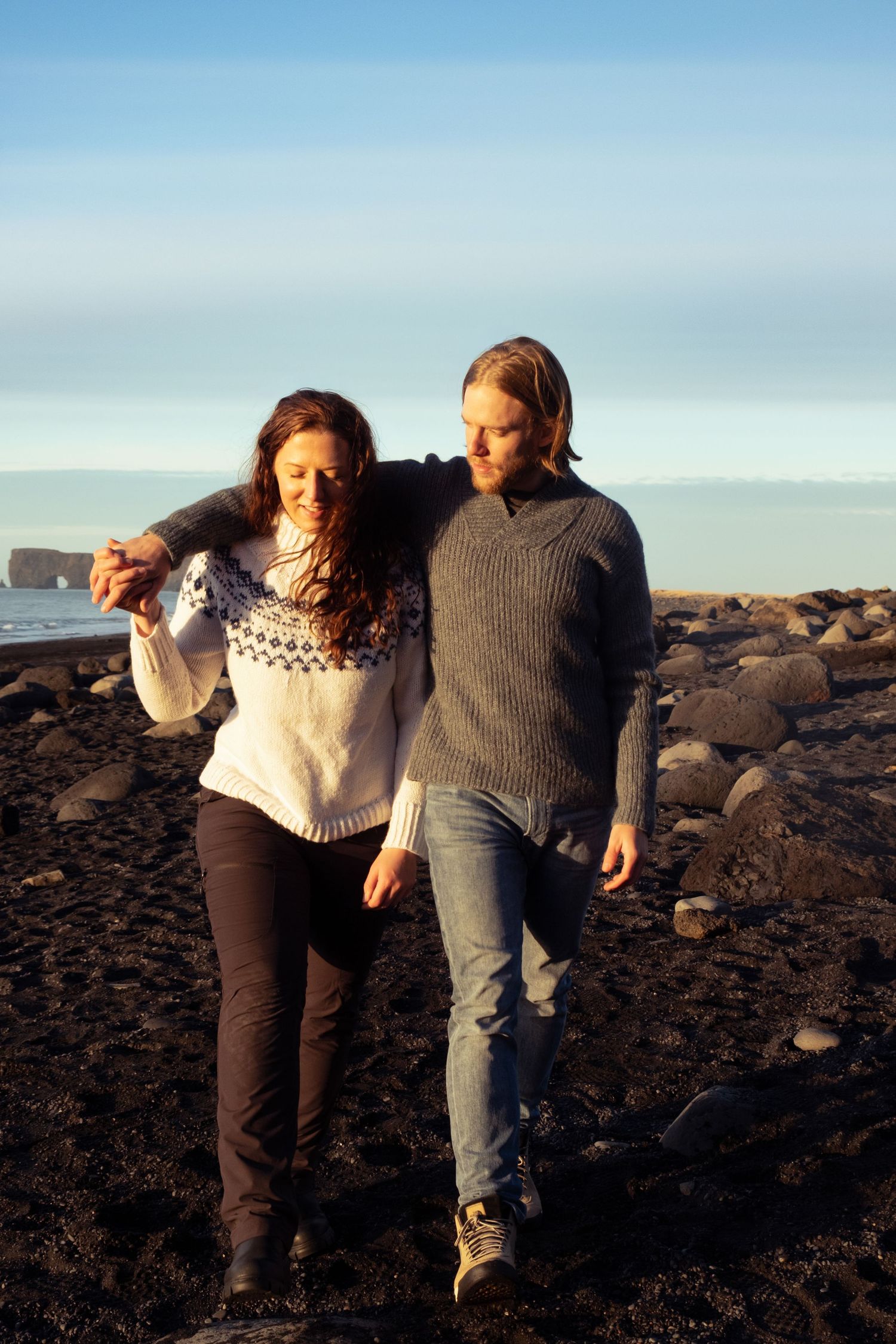 Two people walking together on dark volcanic terrain against a bright blue sky in a sequence of photos.