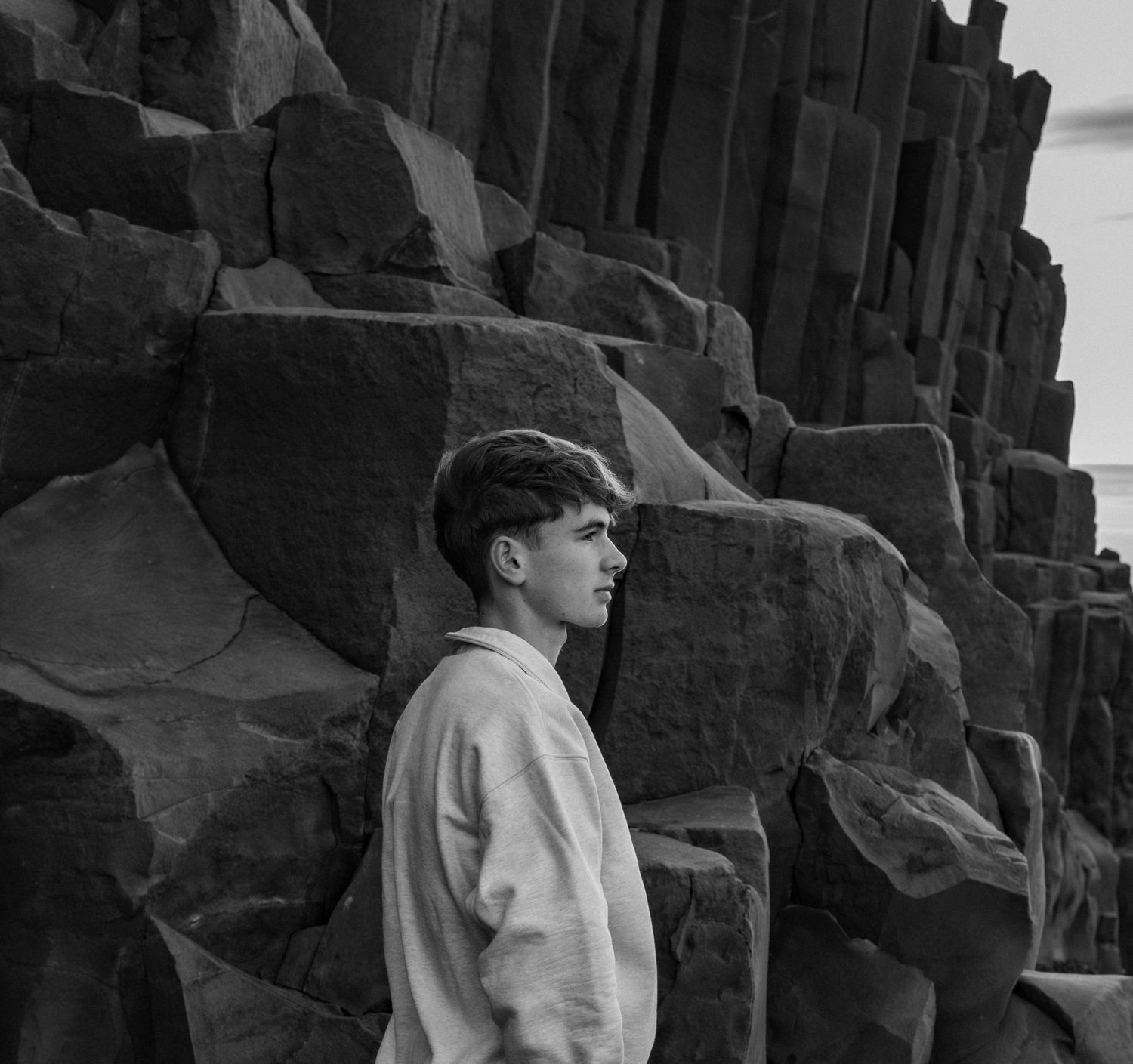 Black and white profile view of a person against a stone wall with dramatic shadows and angular shapes.