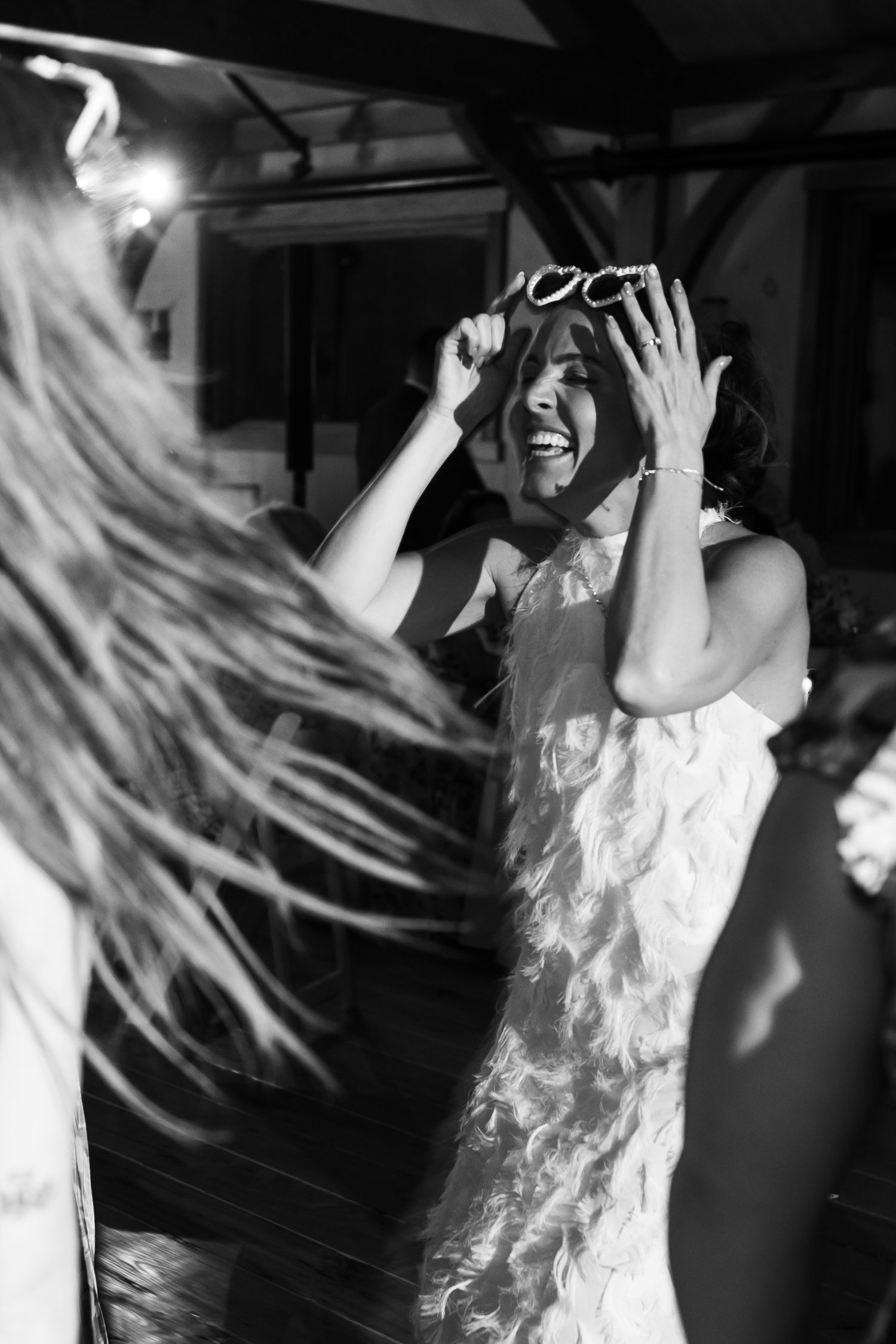 Smiling wedding guest holding sunglasses while dancing at black and white wedding reception.