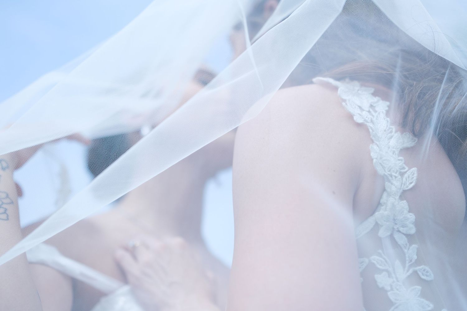 Detail shot of a bride in a lace wedding dress with flowing white veil draping over her shoulders.