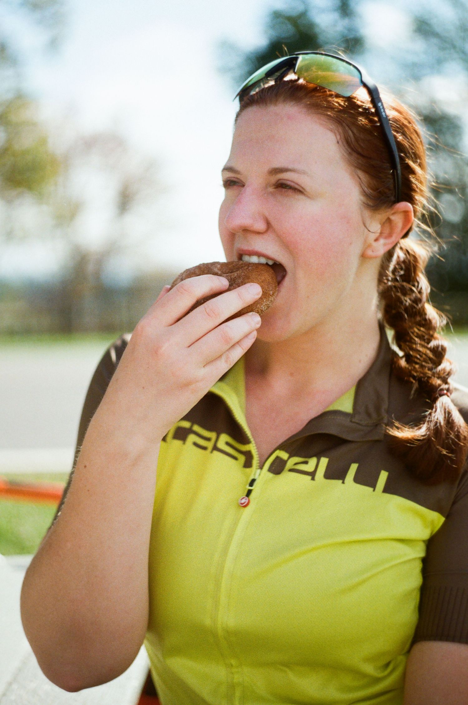 Person in yellow cycling jersey takes a bite of food while enjoying outdoor activity on sunny day.