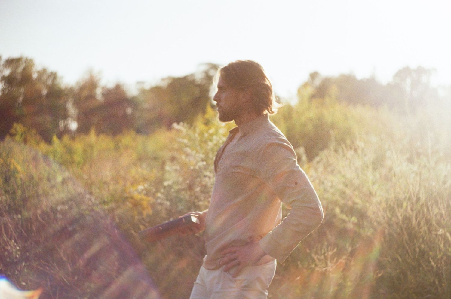 A couple embraces in a golden sunlit field during sunset creating a romantic silhouette against the warm sky.