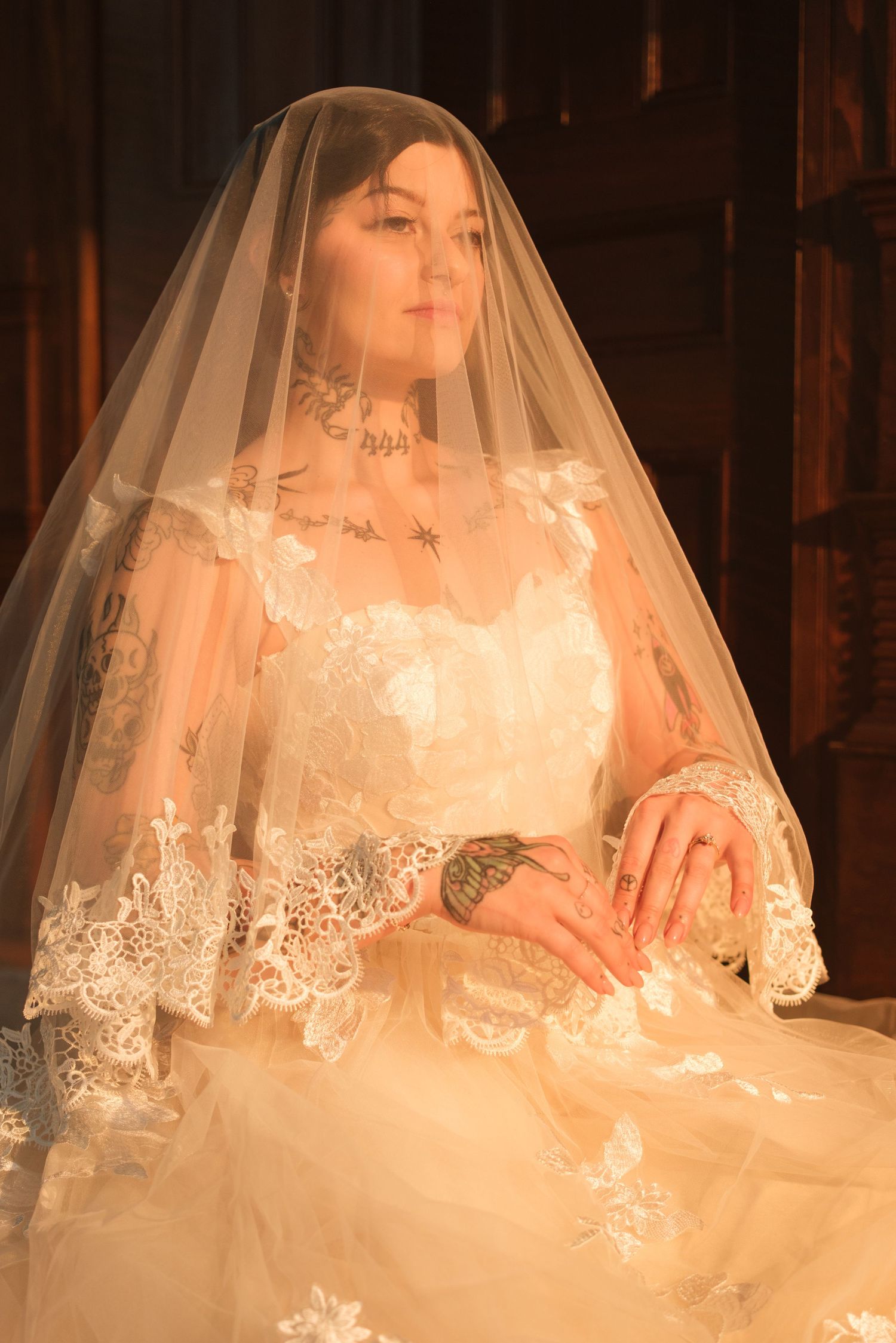 A bride in a white lace wedding gown and veil sits gracefully, bathed in warm golden light.