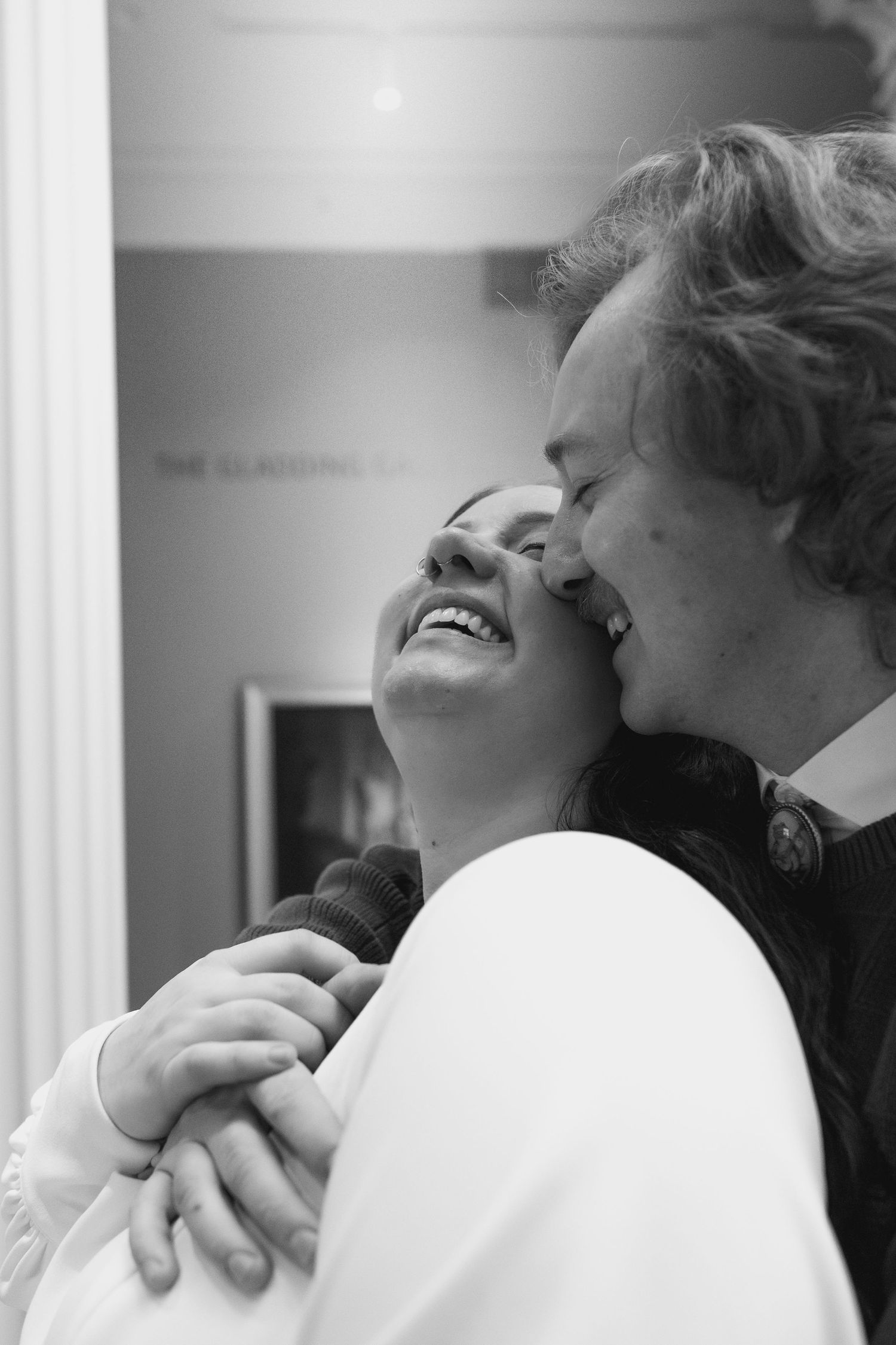 Black and white photo of a couple embracing and laughing together in a tender, joyful moment.