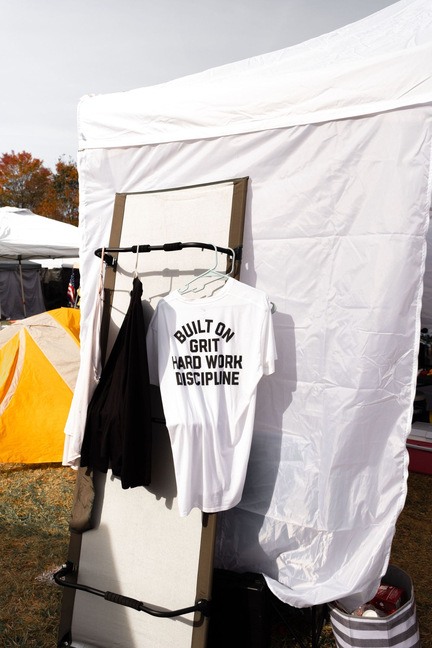 White t-shirts and clothing items hanging on outdoor clotheslines between white tent structures in a field setting.