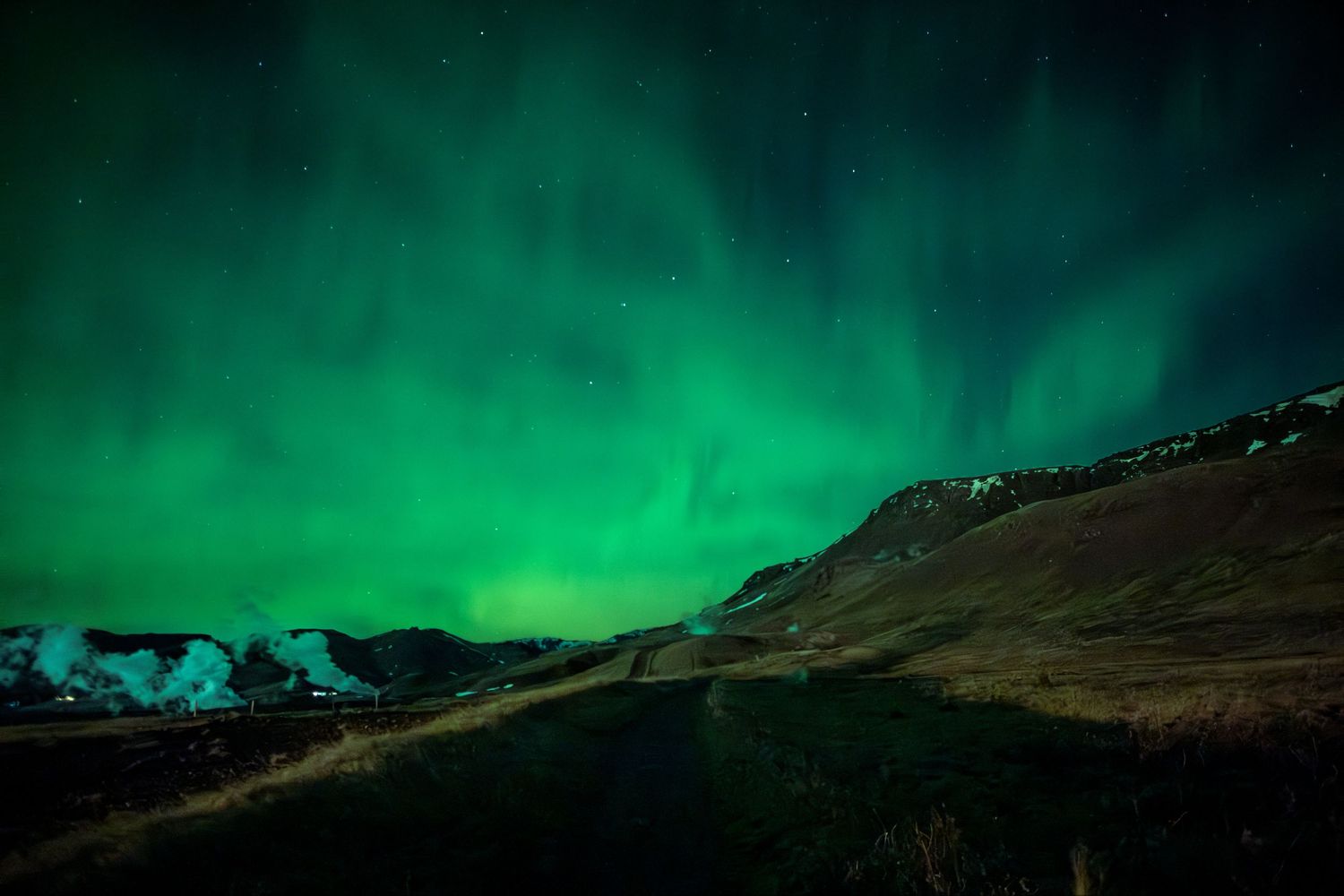 The northern lights dance across a dark sky above silhouetted mountains creating a mesmerizing green aurora display.