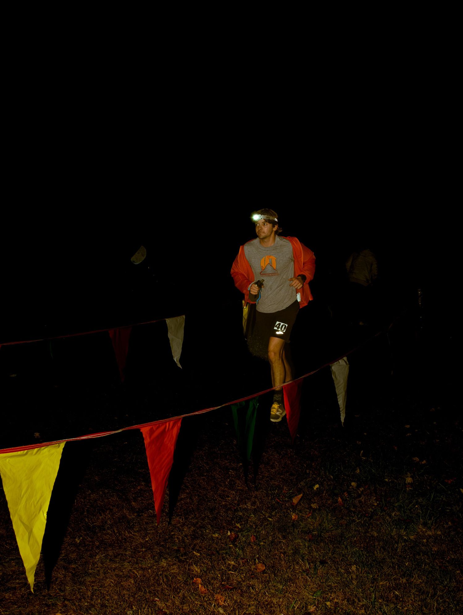 Colorful triangular flags hang on a string at night while people gather in a dimly lit outdoor setting.