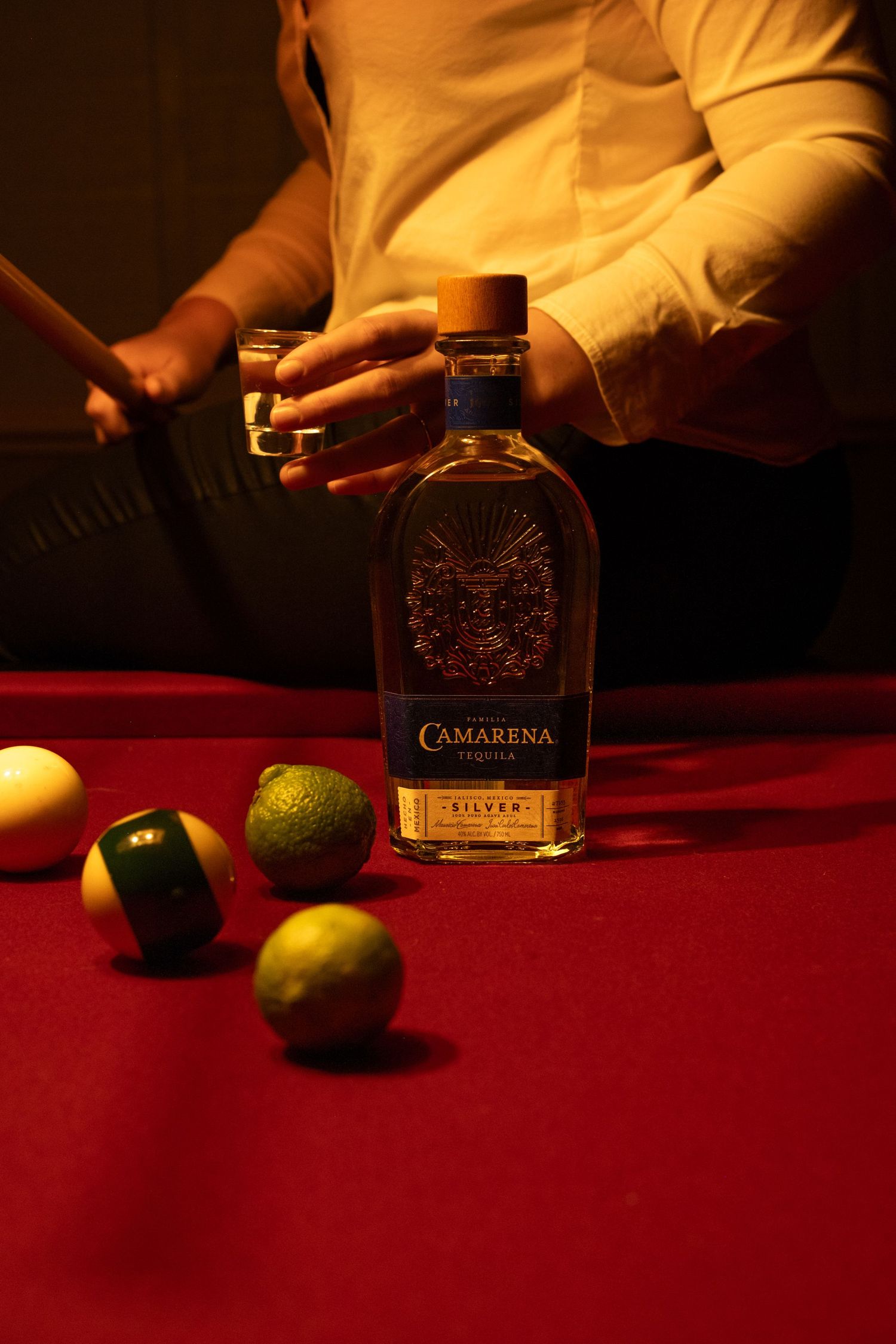 A bottle of Camarena tequila sits on a red velvet surface with limes in dramatic lighting.