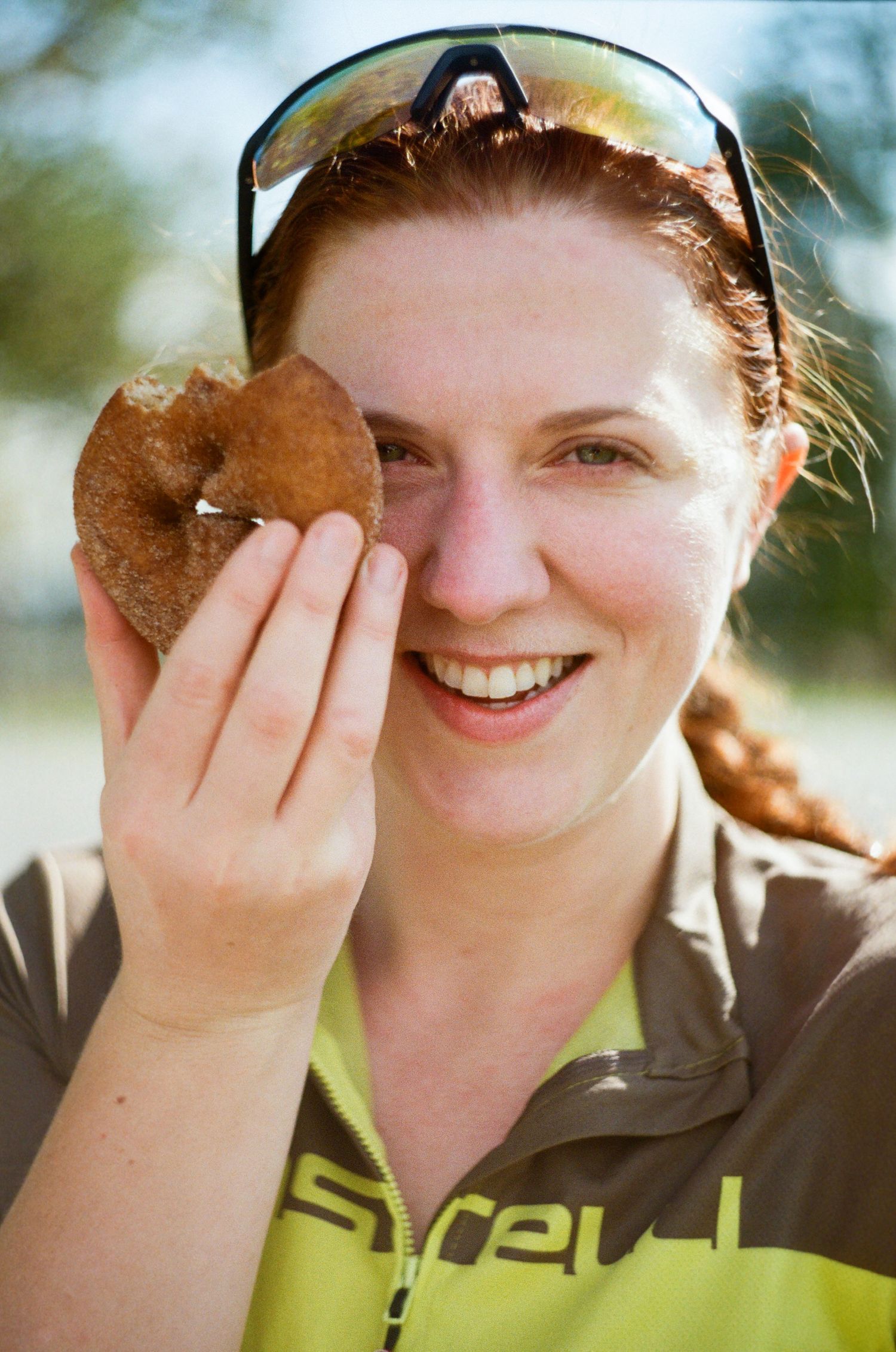 Someone wearing a cycling jersey holds up a heart-shaped leaf while smiling outdoors in natural lighting.