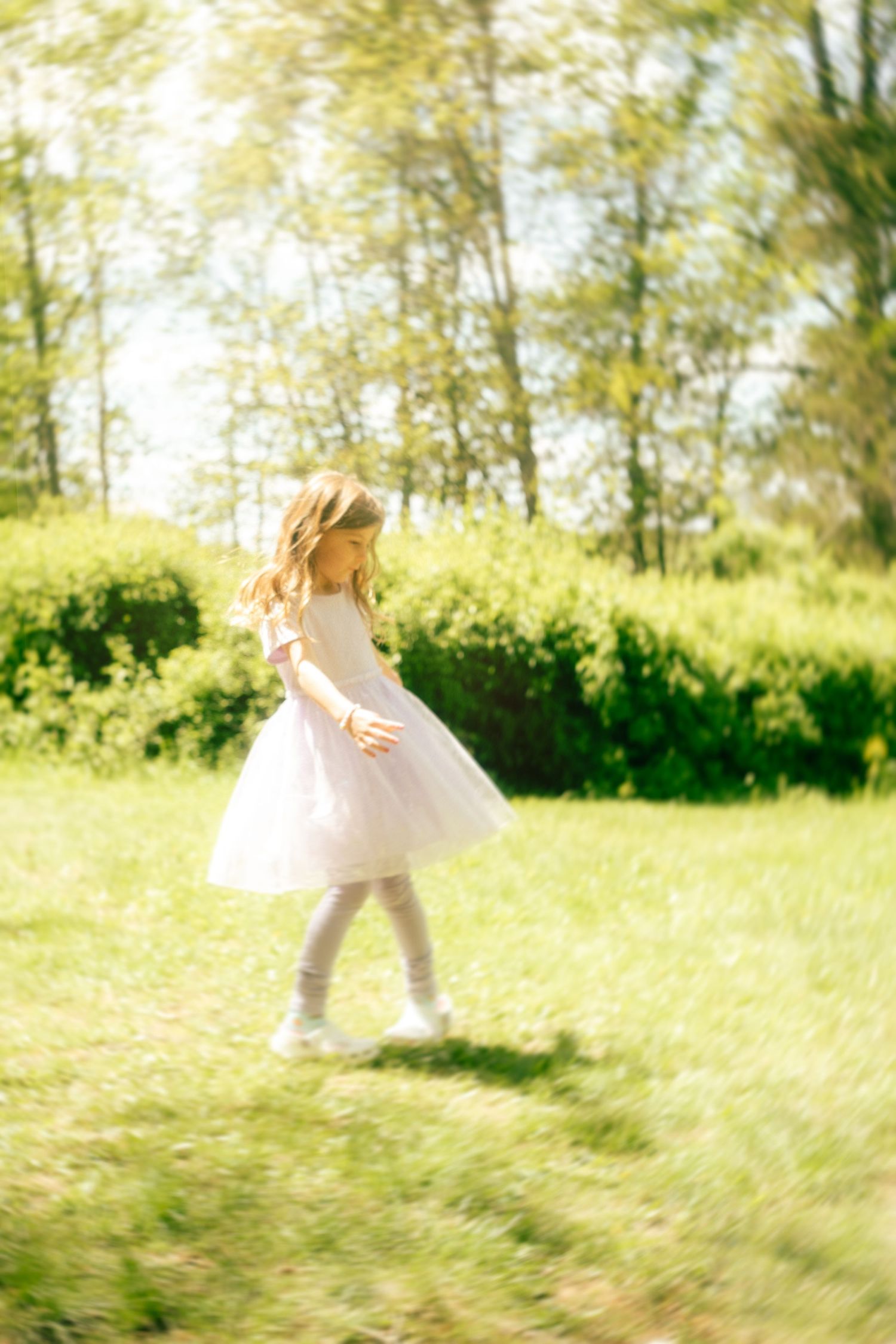 Young girl in white tutu dress twirling in sunny green park, motion blur effect.