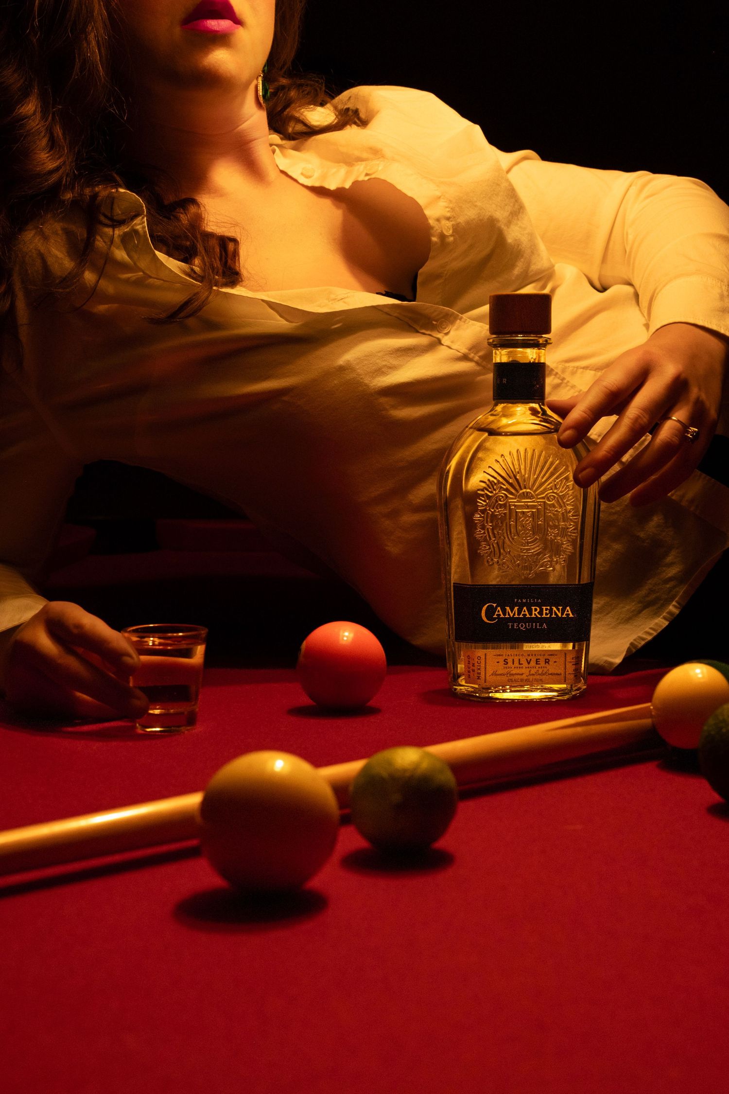 Moody still life series with whiskey bottle and fruit on red table in dramatic lighting.