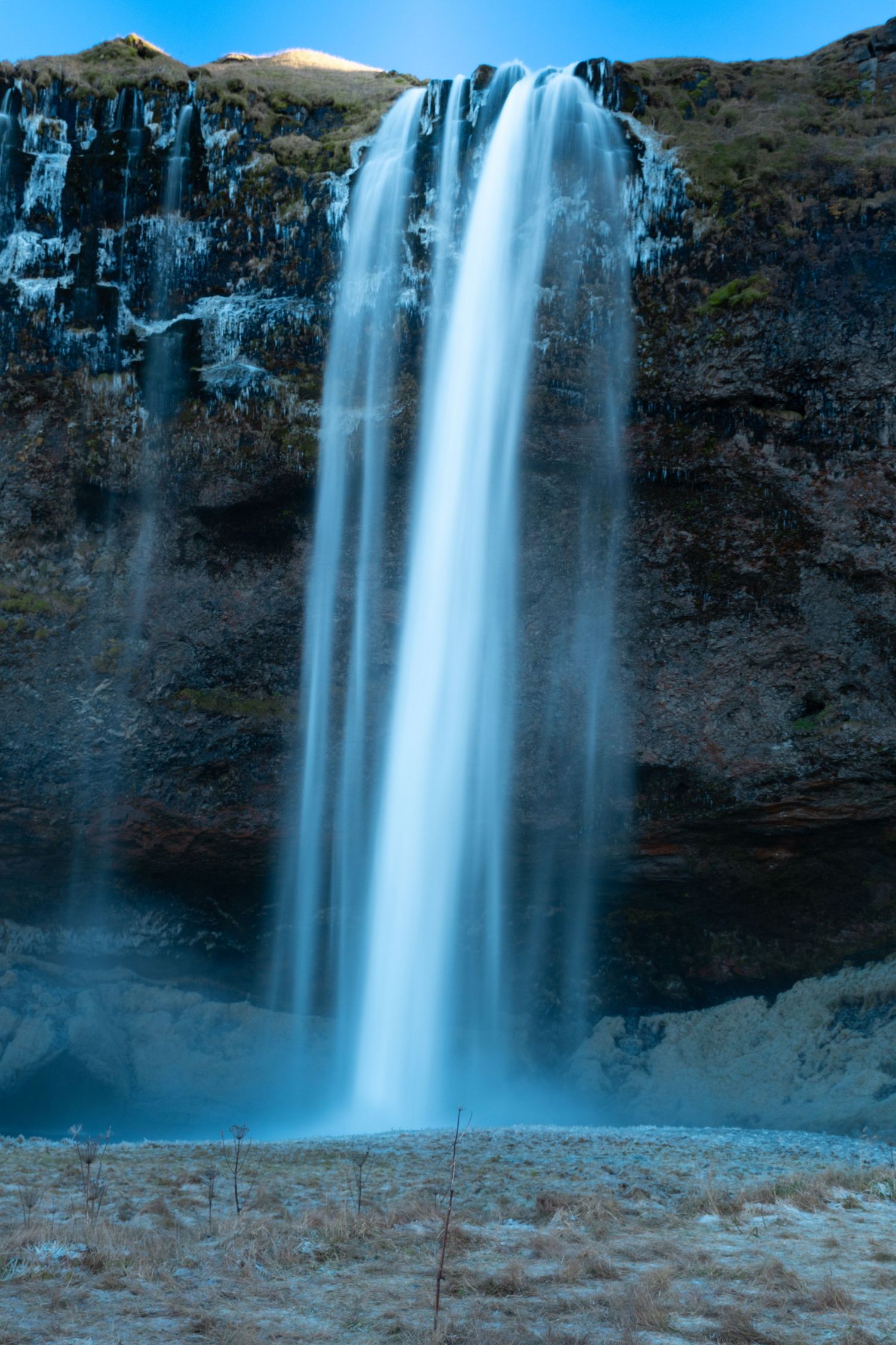 Majestic Seljalandsfoss waterfall cascades down moss-covered cliffs in Iceland during winter with snow-capped peaks.