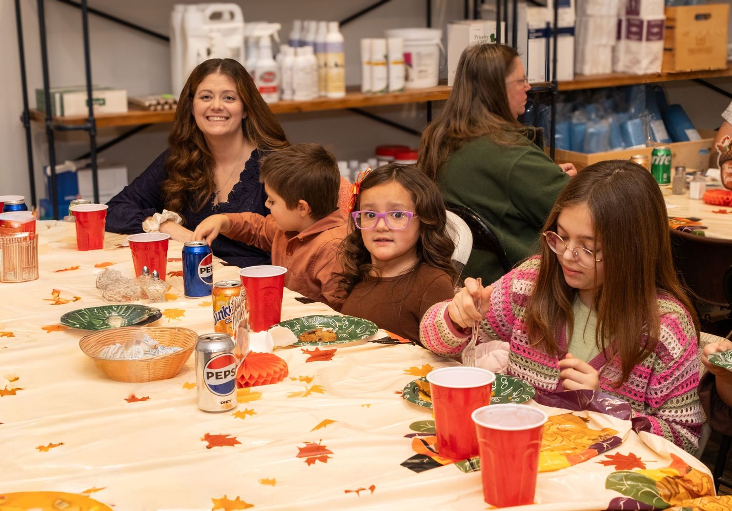 Students gather around tables decorated with fall-themed tablecloths during a classroom celebration event.