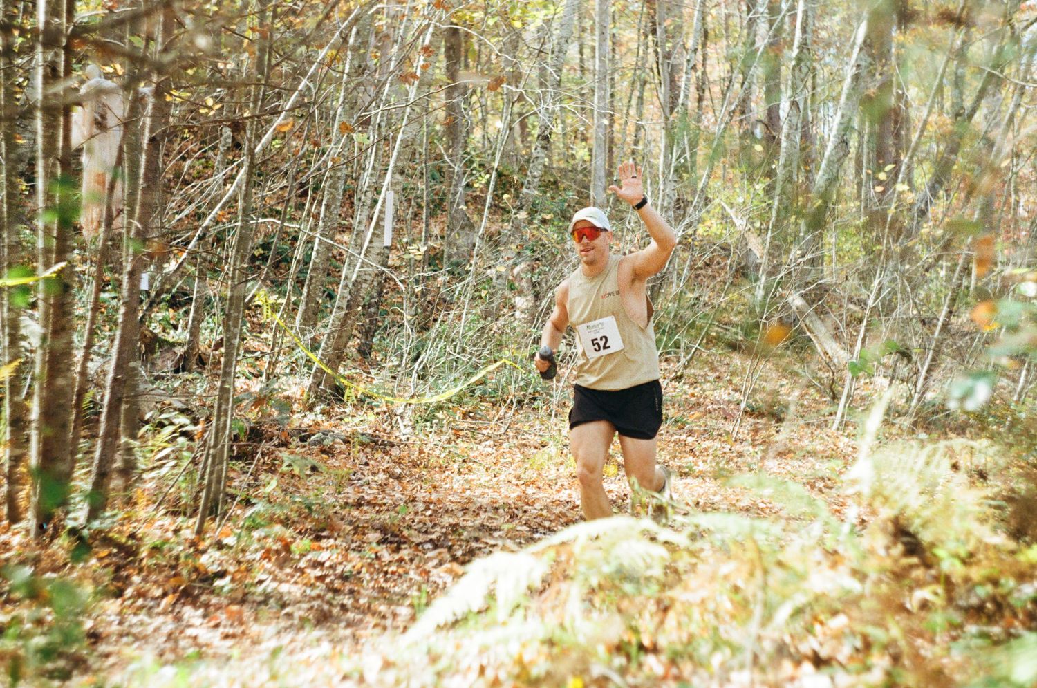 Runner navigates through a wooded trail course covered in autumn leaves during a cross country race.
