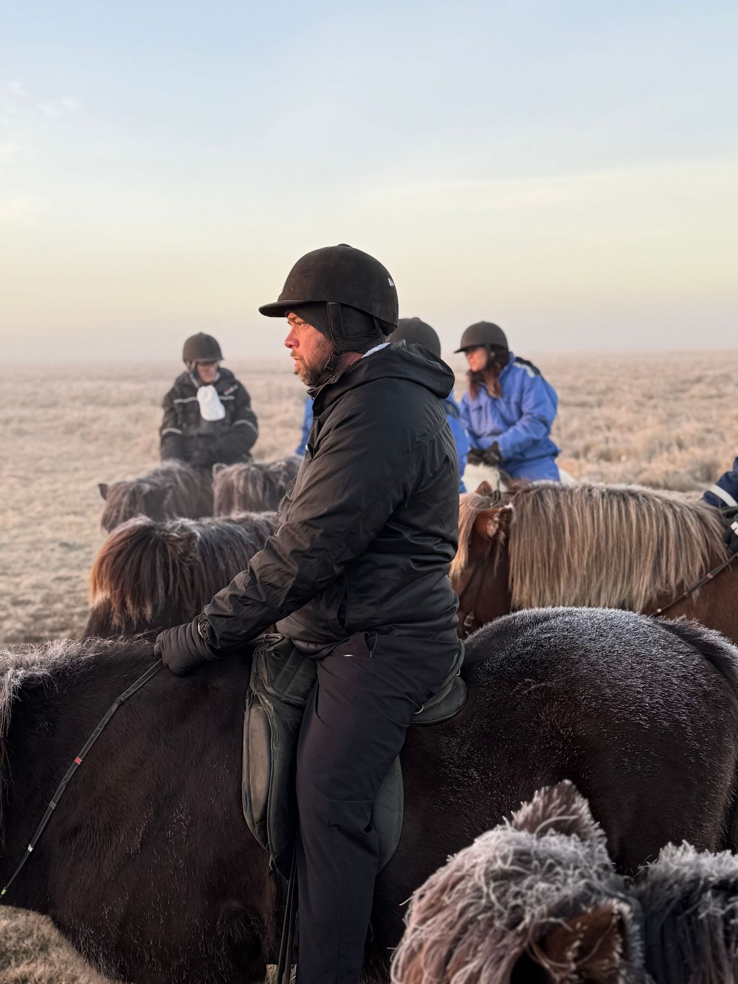 Riders mounted on dark horses traverse a misty winter landscape during a group trail ride.