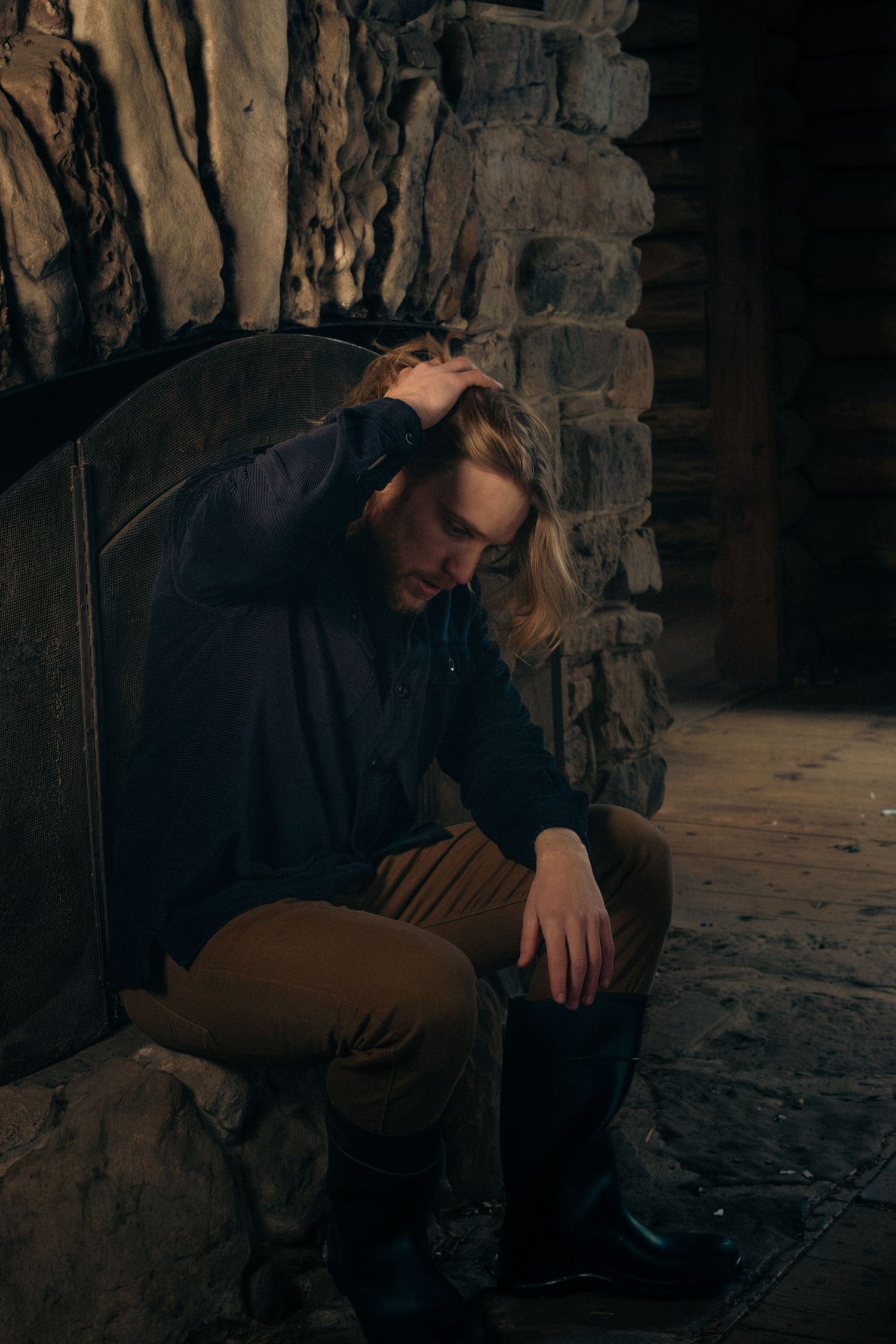 A person sits alone in a dark stone corridor, appearing distressed and hunched over in a contemplative pose.