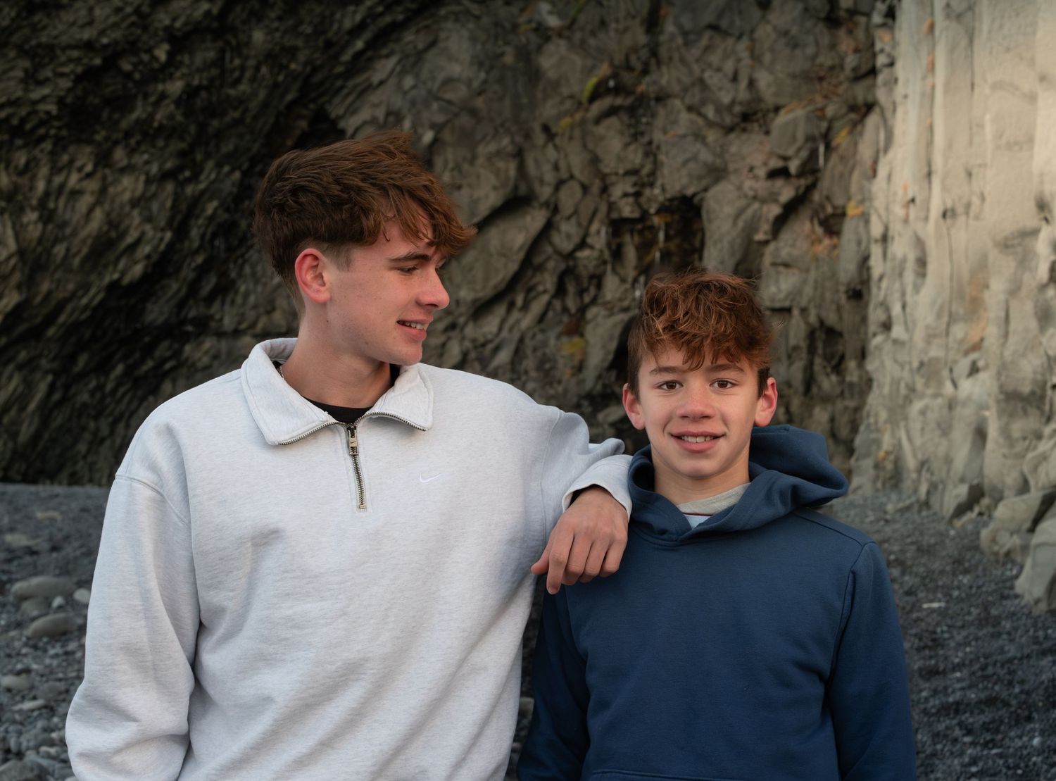 Two people in casual attire sit together against a rocky backdrop during an outdoor photoshoot.