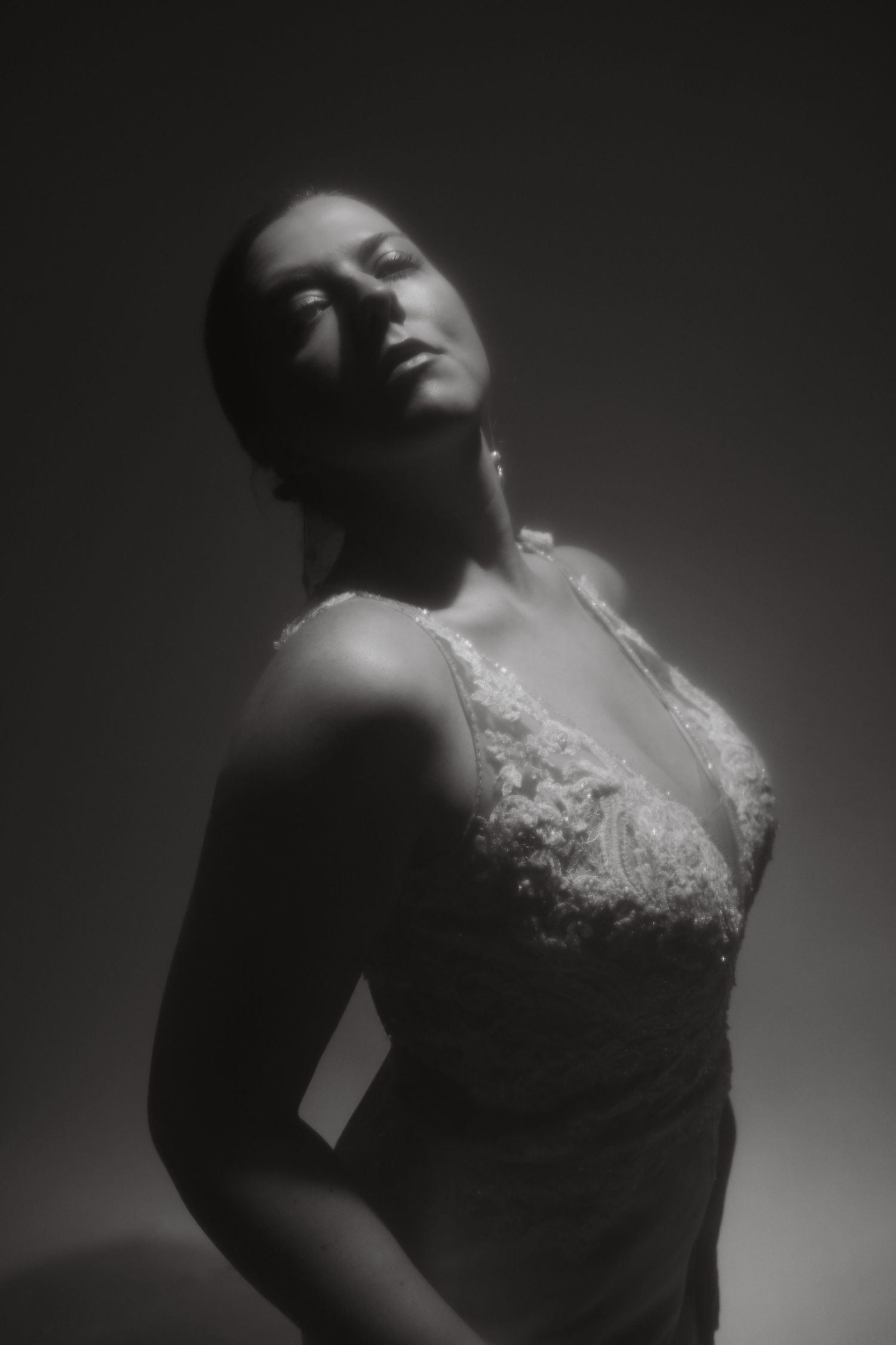Dramatic black and white portrait of figure in lace dress with head tilted back in moody lighting.