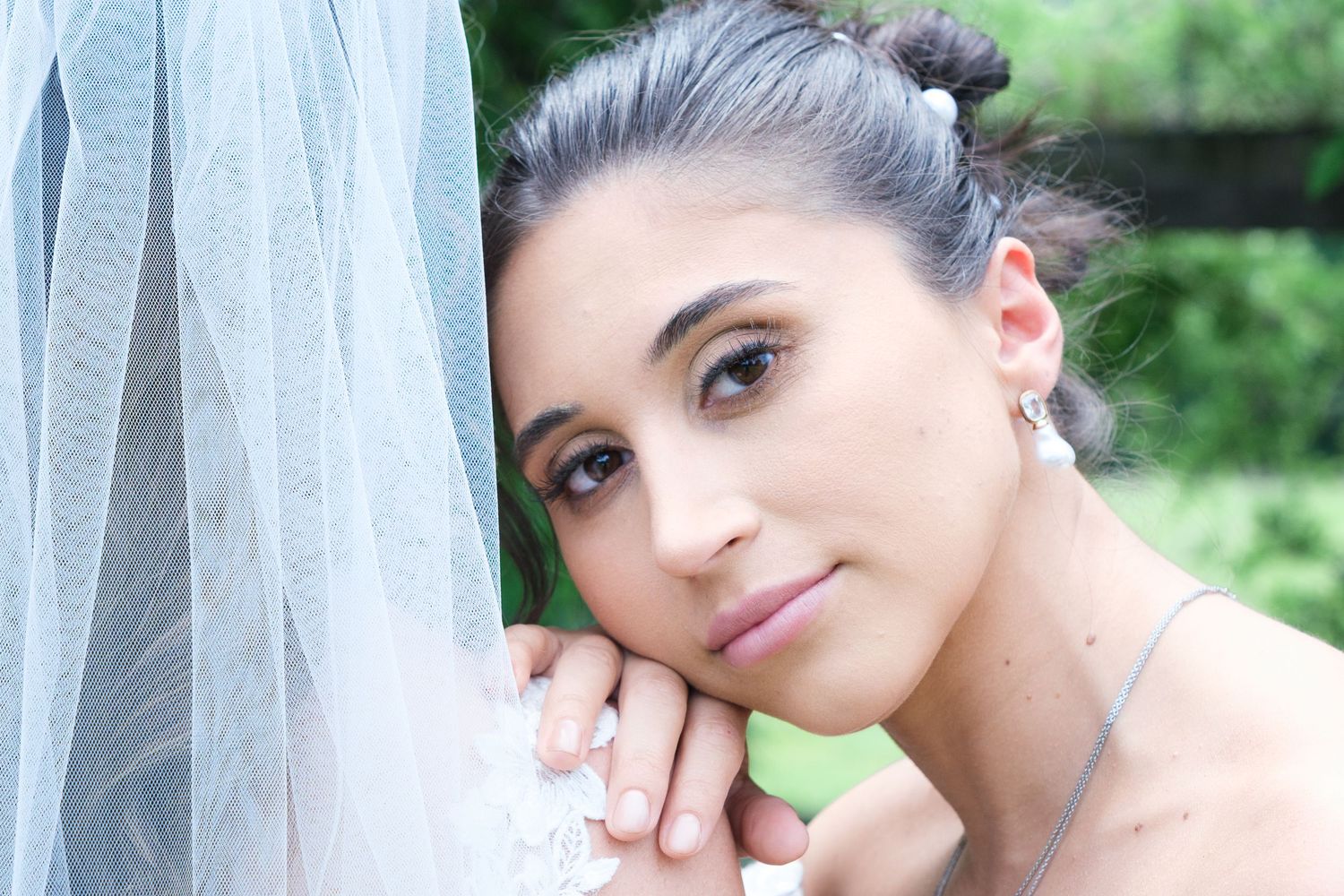 Close-up portrait of a beautiful bride with elegant updo hairstyle, wearing a veil and delicate earrings outdoors.