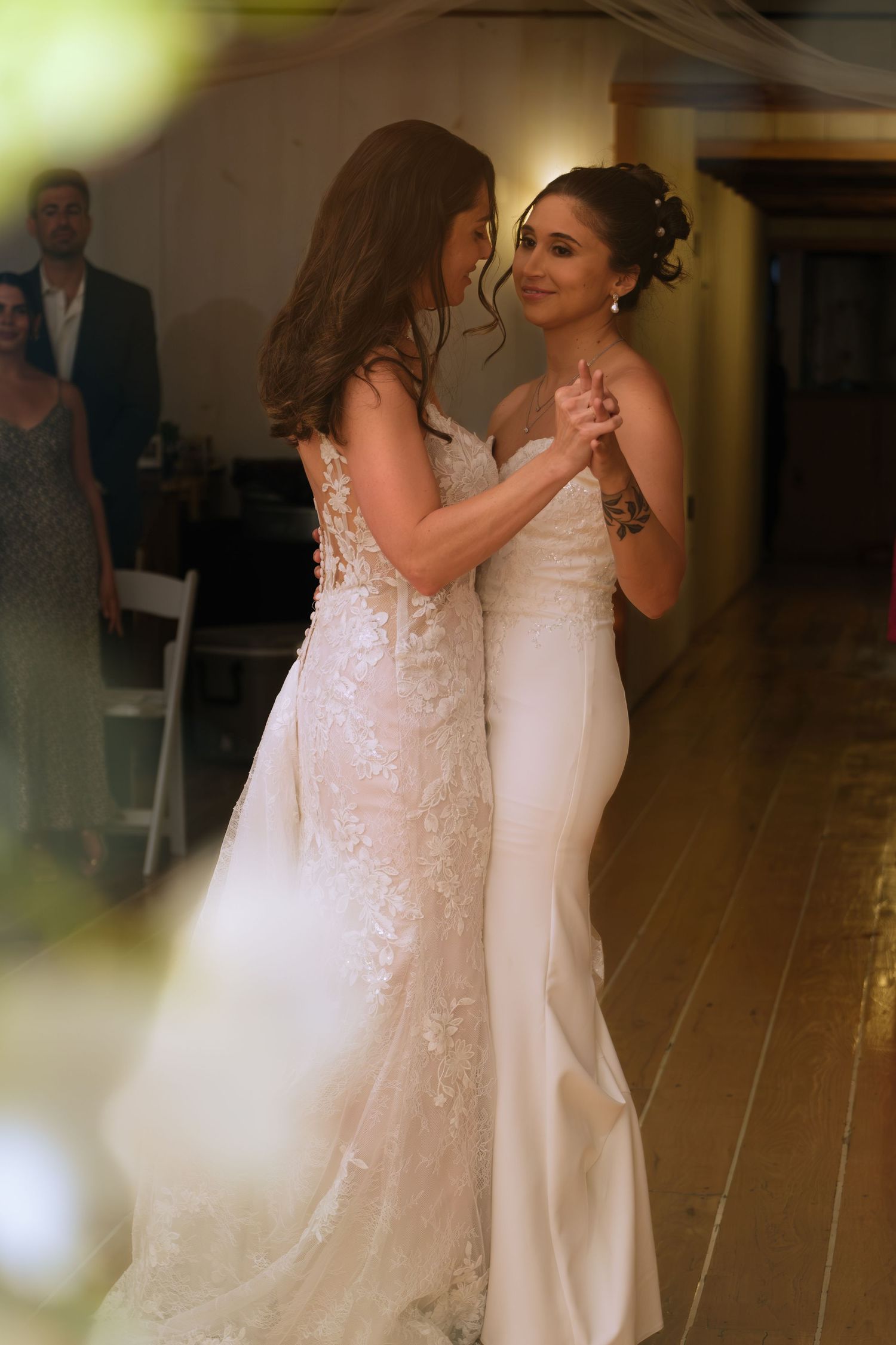 Two women in white wedding gowns share a first dance at a wedding reception.