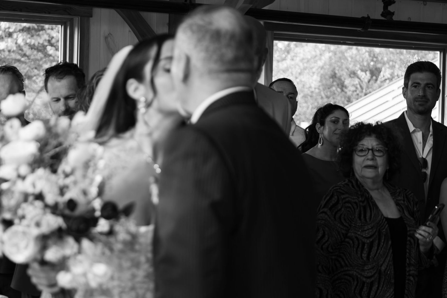 Black and white wedding ceremony photo showing bride and groom at altar with emotional guests watching in background.