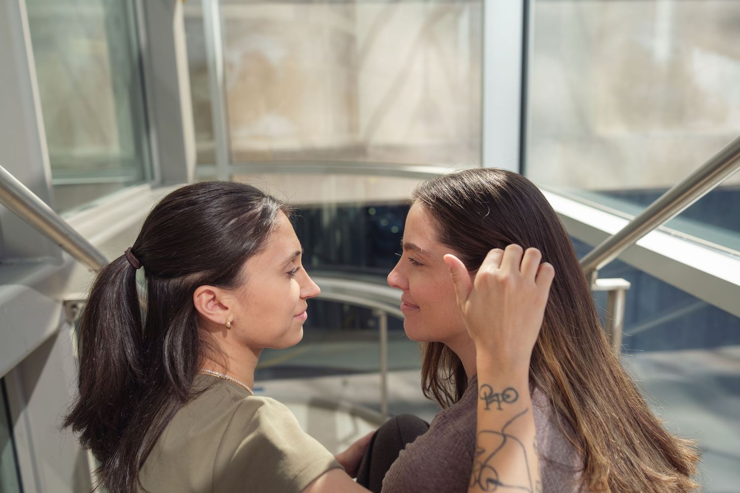 Two people share an intimate moment in a sunlit corner, with one gently touching the other's hair.