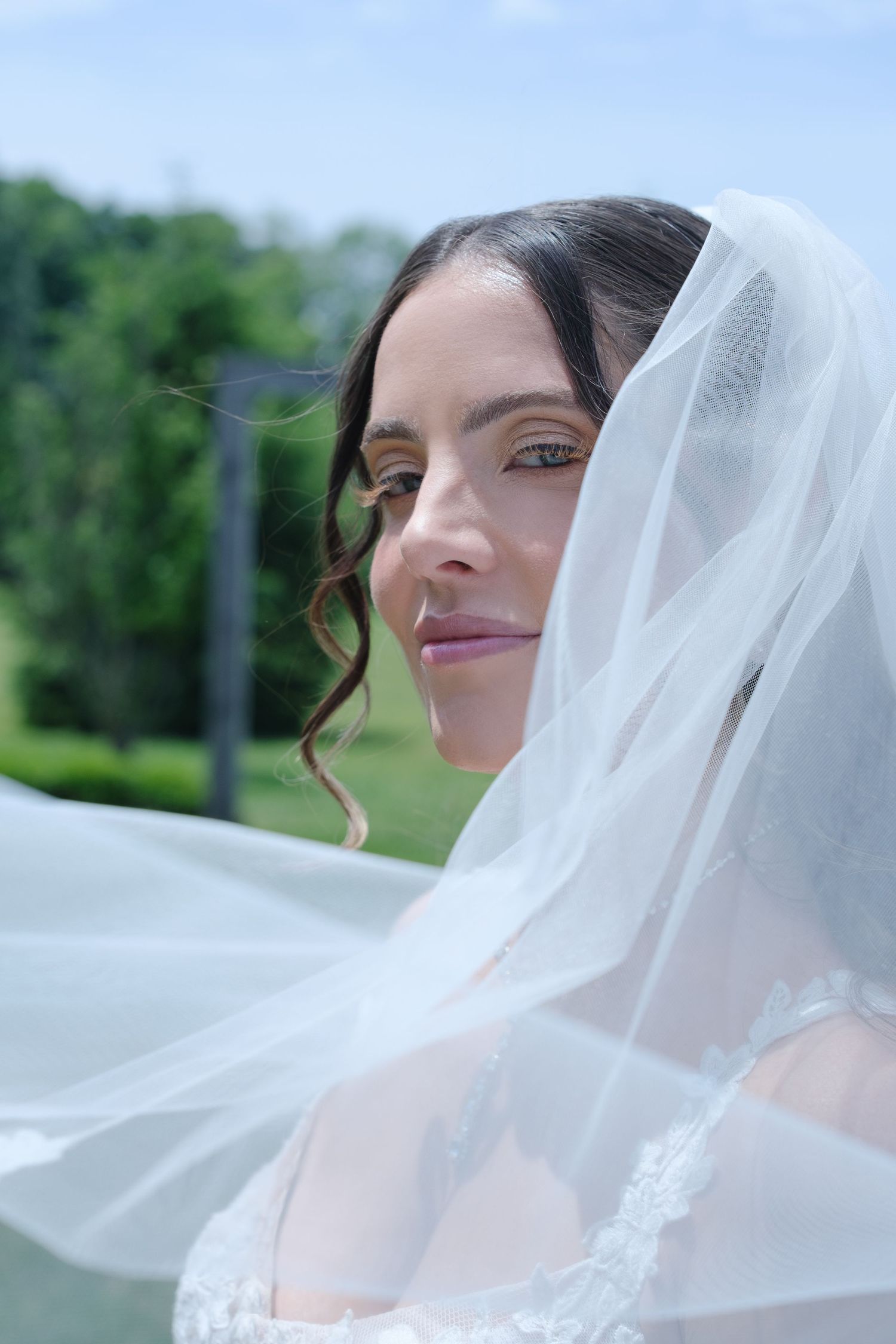 Beautiful bride with updo hairstyle draped in a flowing white veil outdoors.