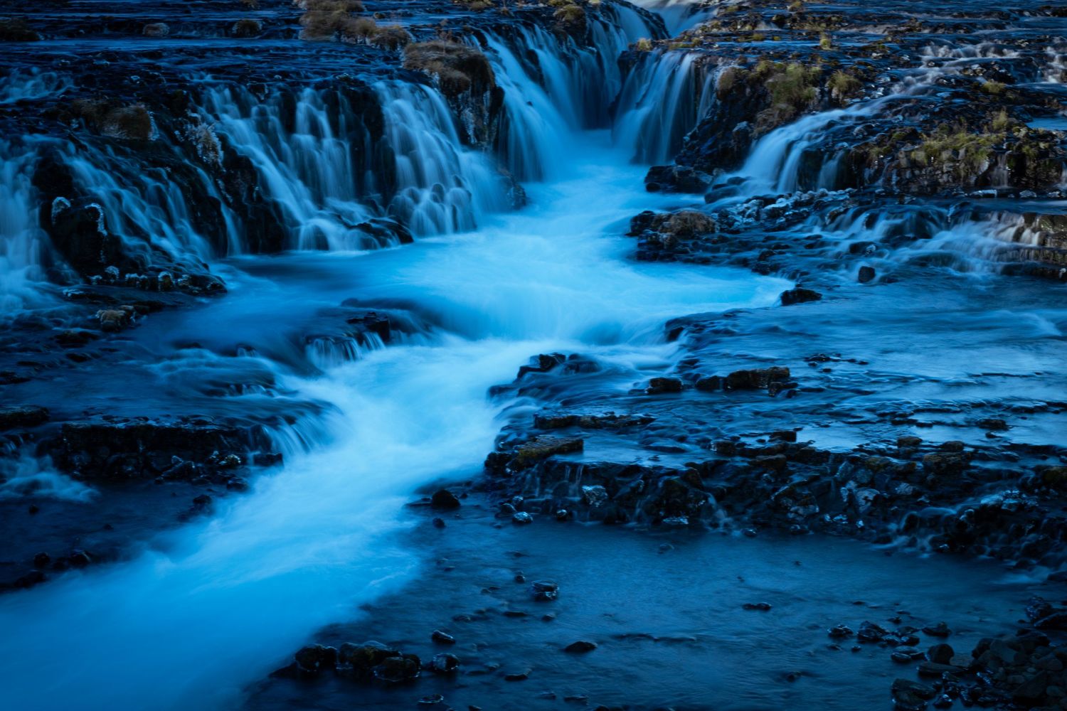 Long exposure waterfall cascading over dark rocks creates ethereal blue streams in low light conditions.