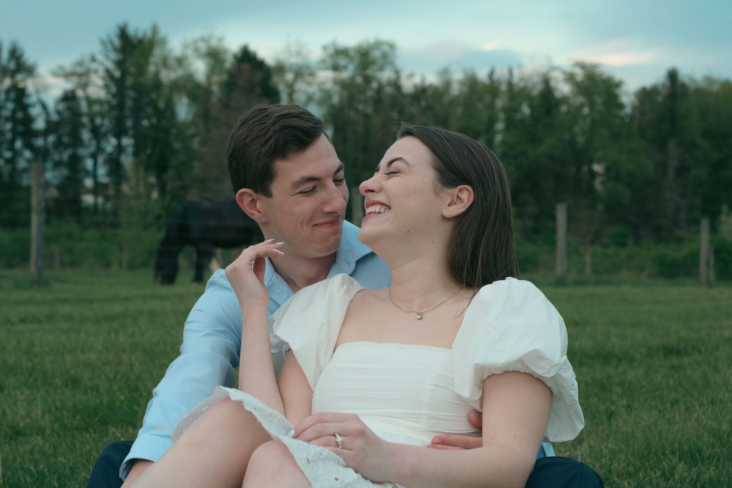 A young couple sitting together in a green field, smiling and gazing at each other on a romantic outdoor date.