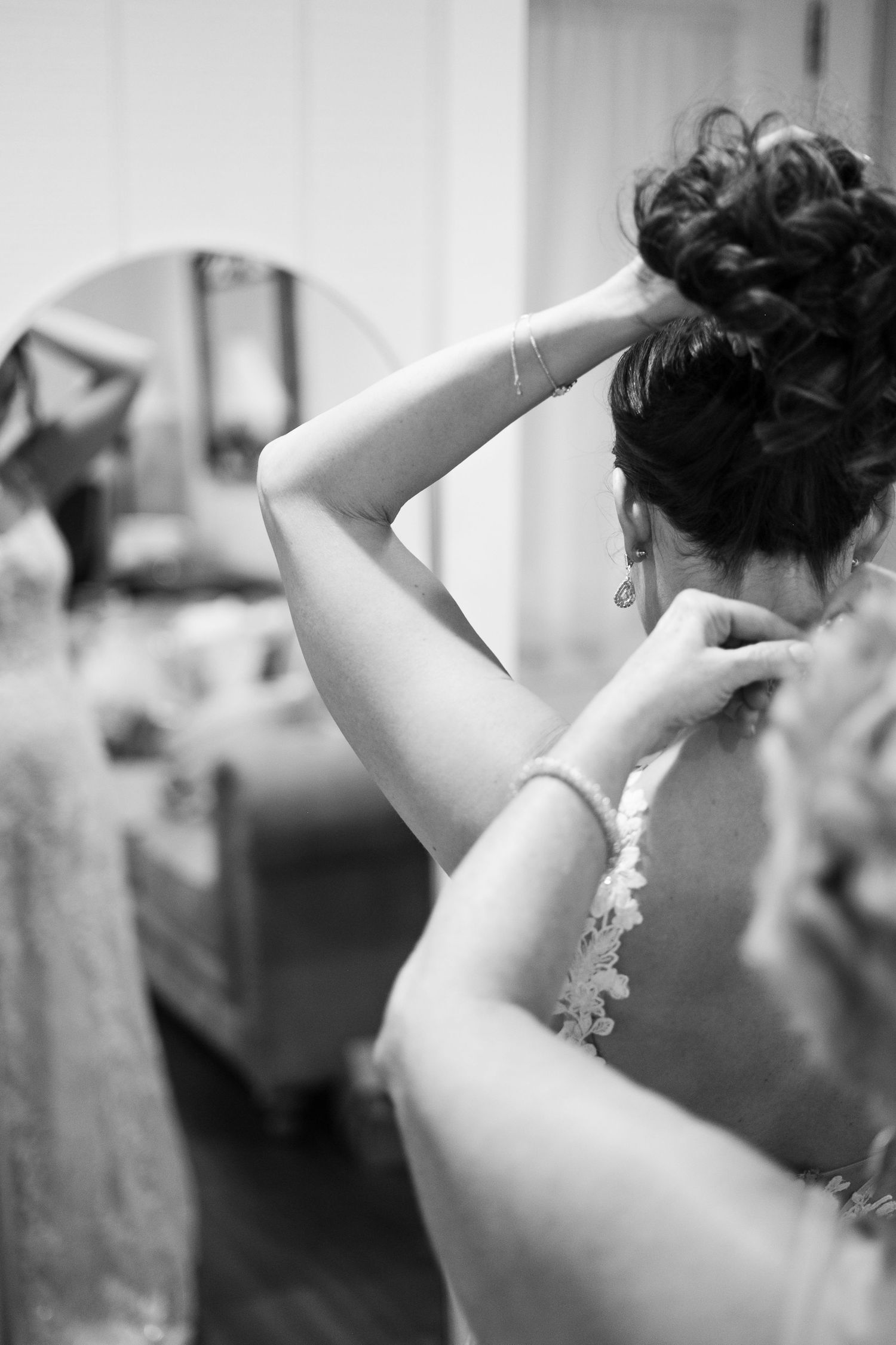 Bride getting dressed with bridesmaid fastening wedding gown, captured in elegant black and white photography.