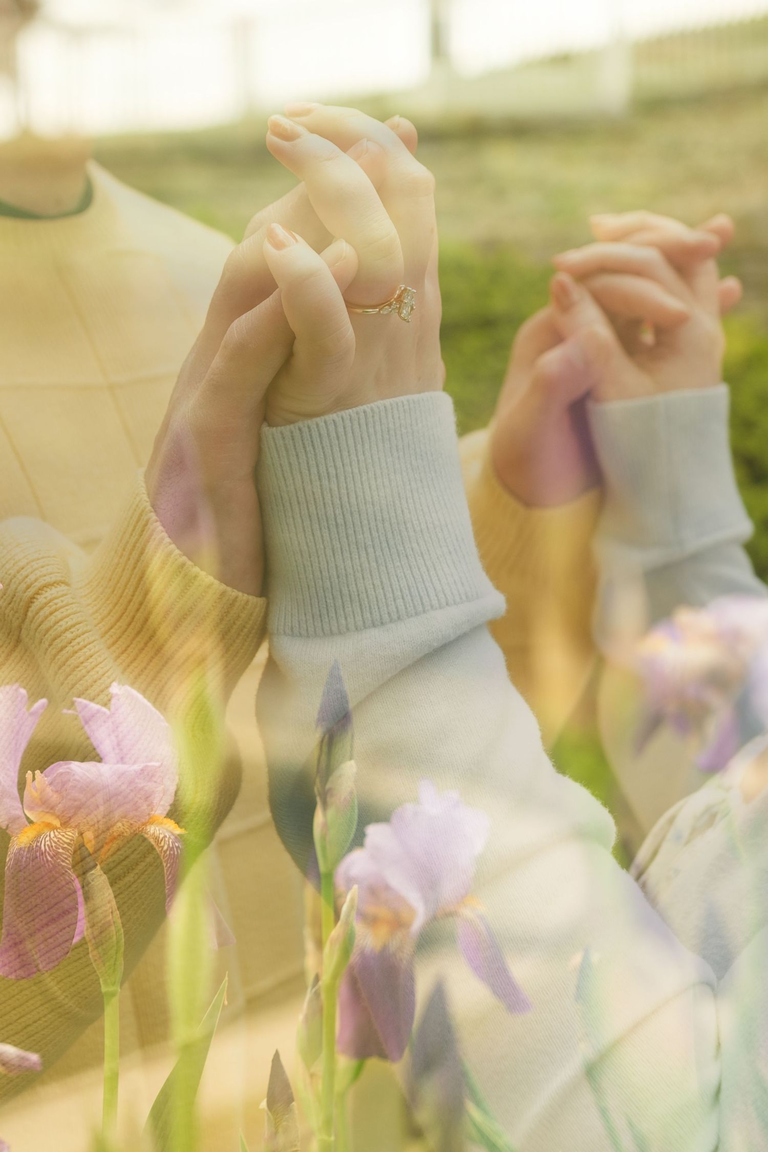 Two people holding hands outdoors with a dreamy double exposure of purple iris flowers in soft pastel tones.