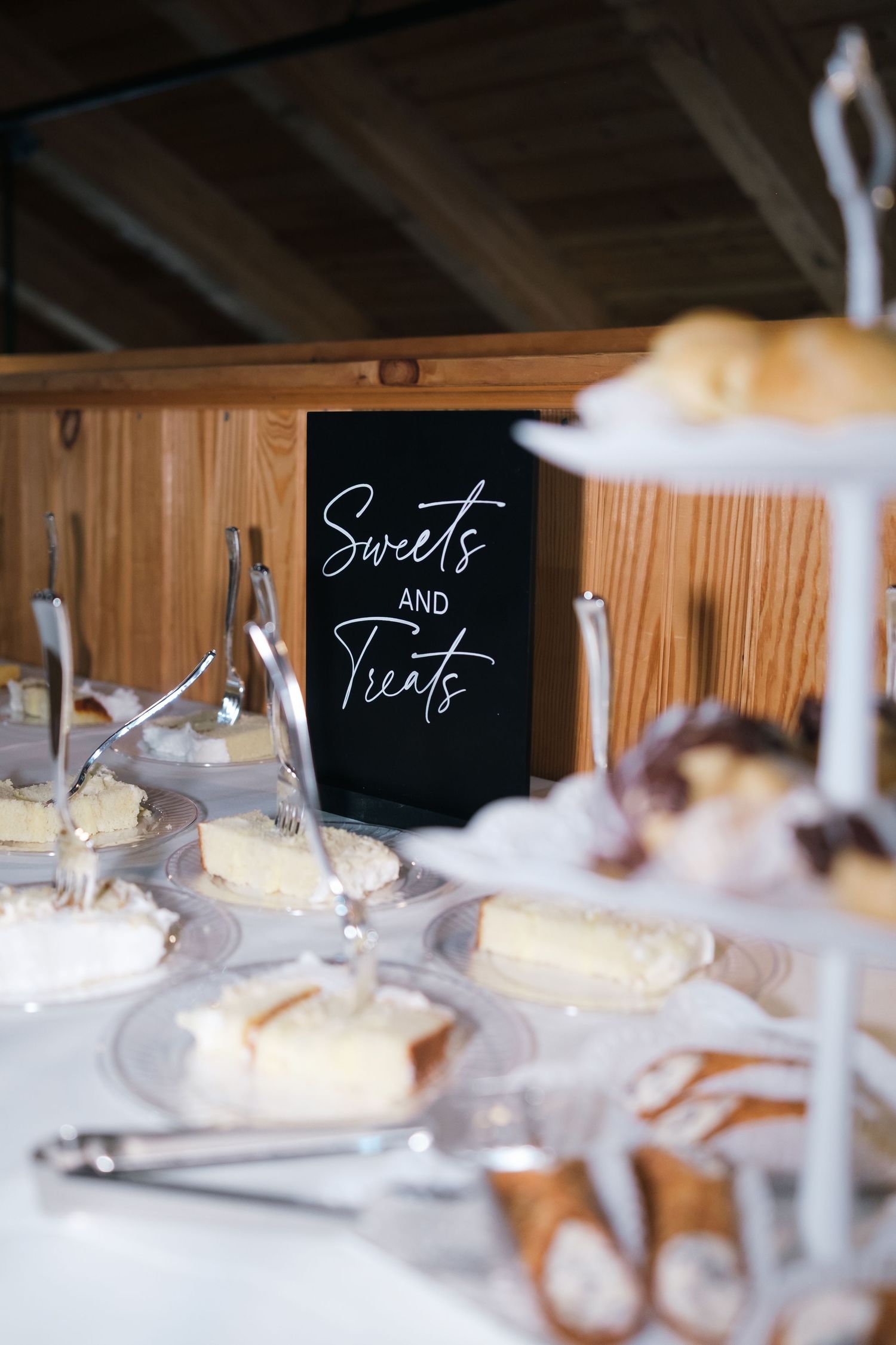 Elegant wedding dessert table with a black Sweets and Treats sign surrounded by cakes and pastries.