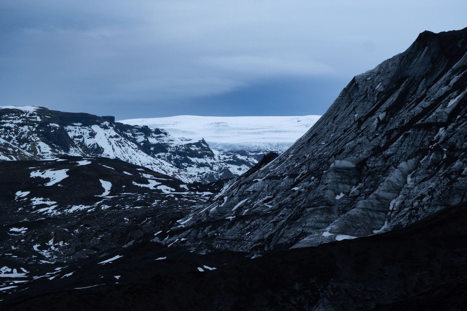 A dramatic panoramic view of snow-covered mountain peaks and ridges under a moody cloudy sky.