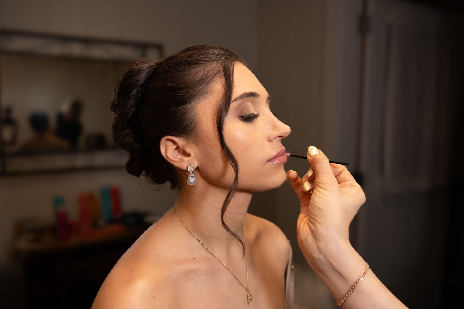 Bride getting lipstick applied by makeup artist during bridal beauty preparation session.