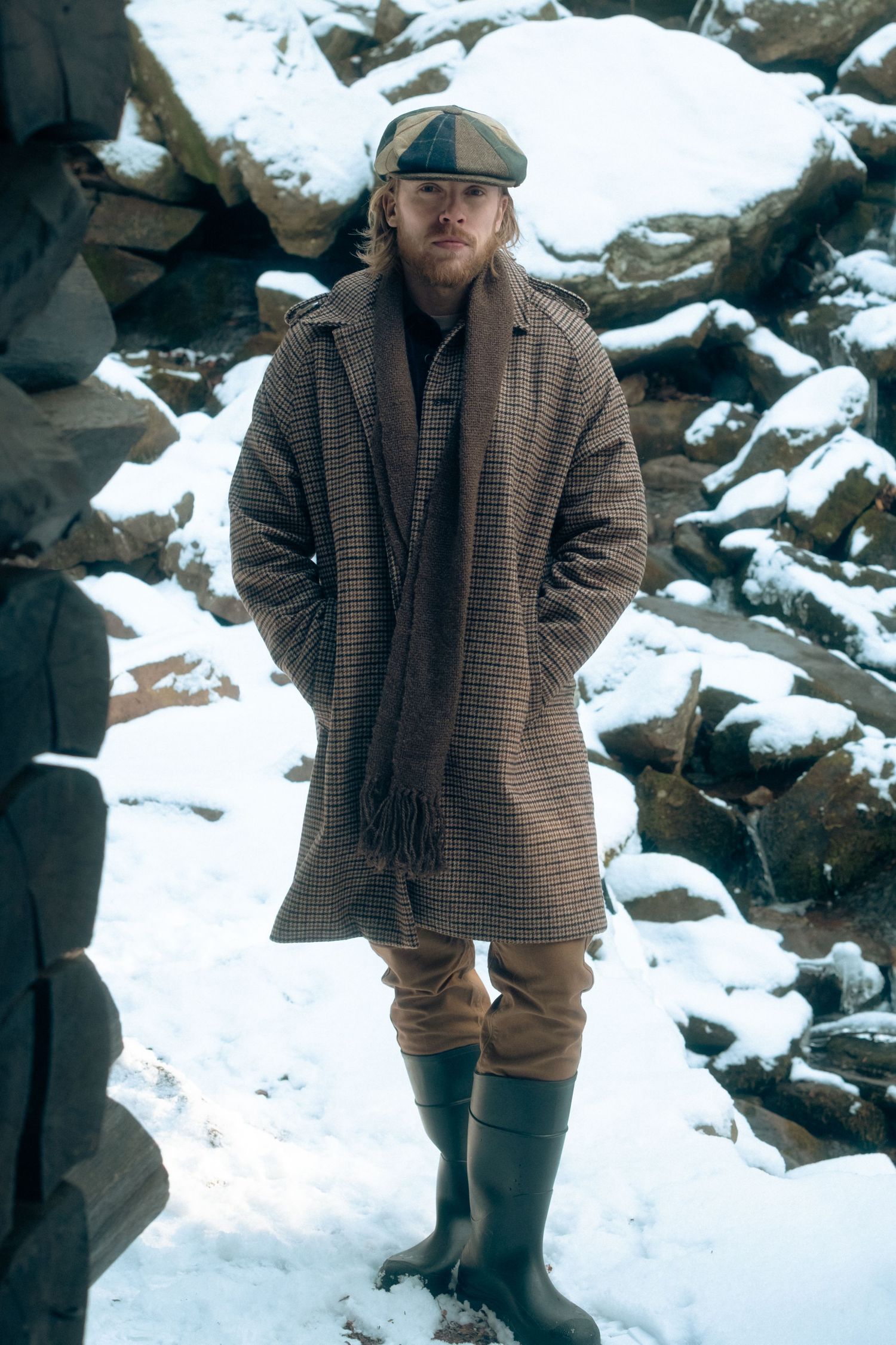 Person wearing winter clothing stands in snowy landscape with rocky outcrops visible in background.