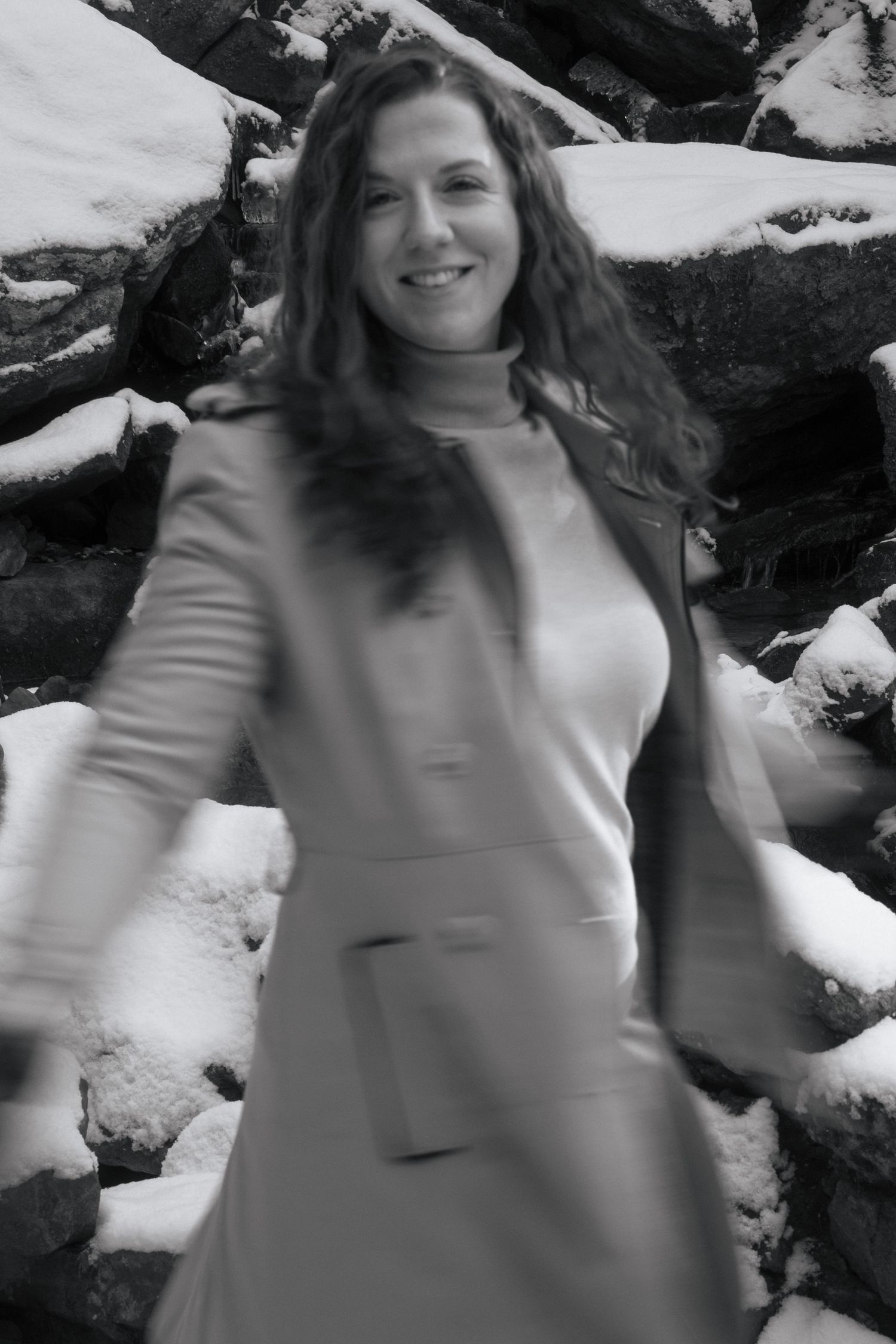 A person in a light-colored coat poses against a snowy background in a black and white photograph.