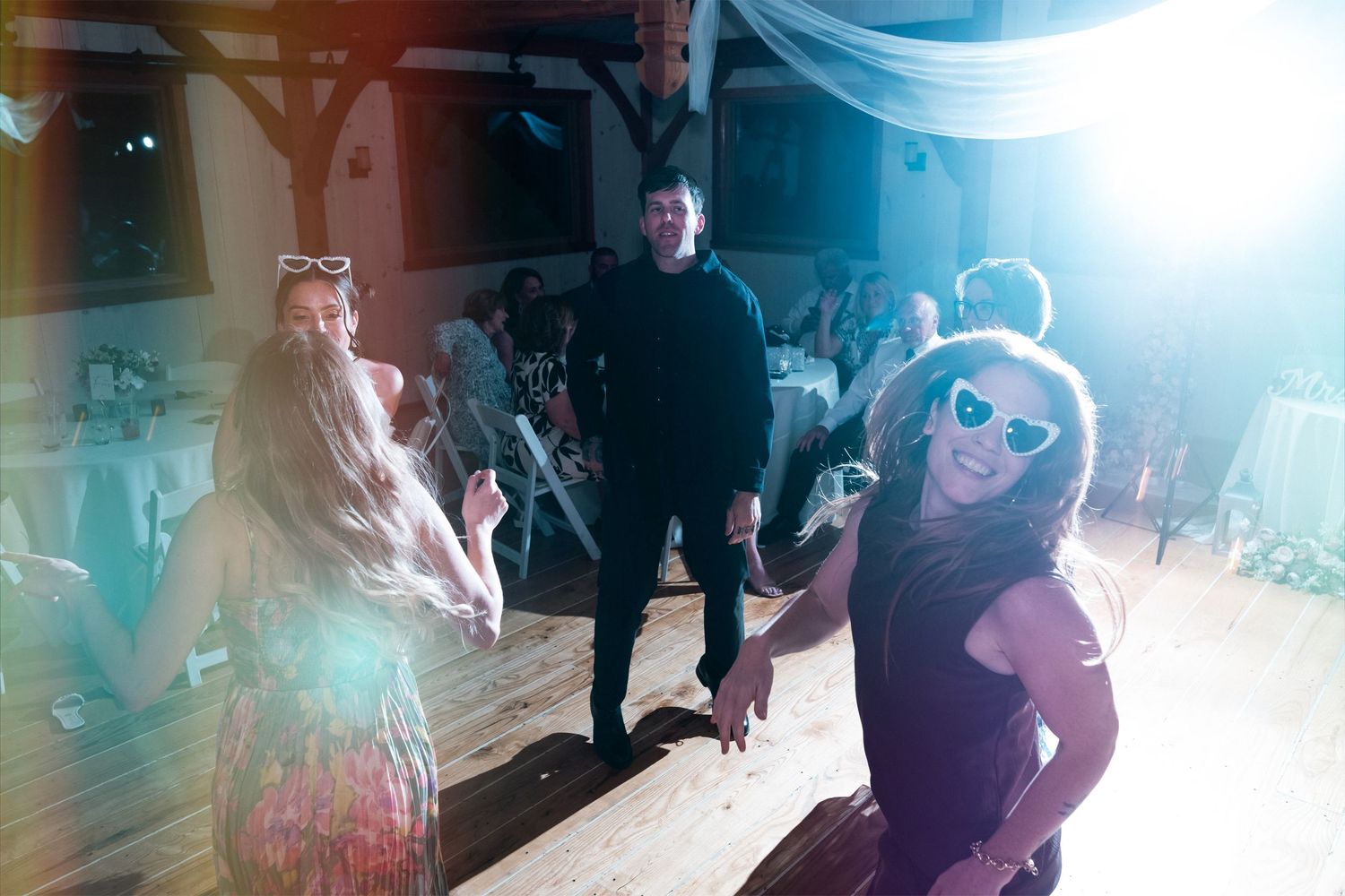Guests dancing and celebrating at an indoor wedding reception with bright lights and festive atmosphere.