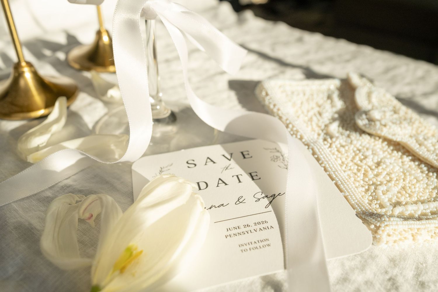 Elegant wedding invitations and envelopes arranged with delicate white flowers and ribbons on a textured beige surface.