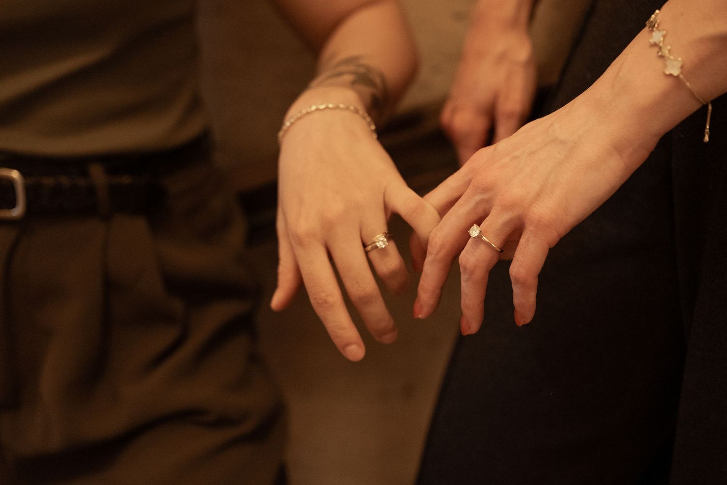 A series of hands showing off engagement rings and wedding bands against a dark background.