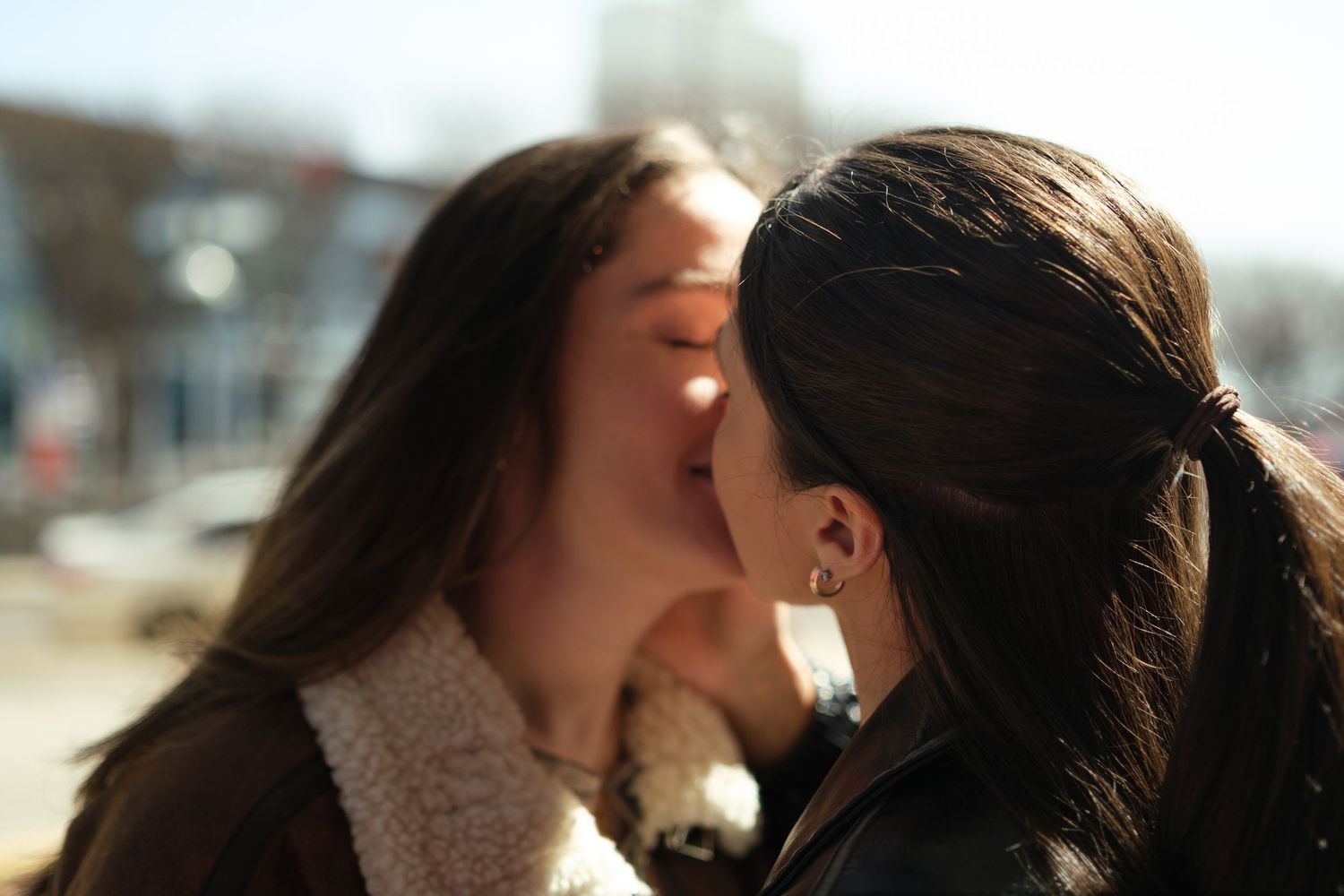 A couple shares a tender kiss in warm sunlight while leaning against a wooden railing outdoors.